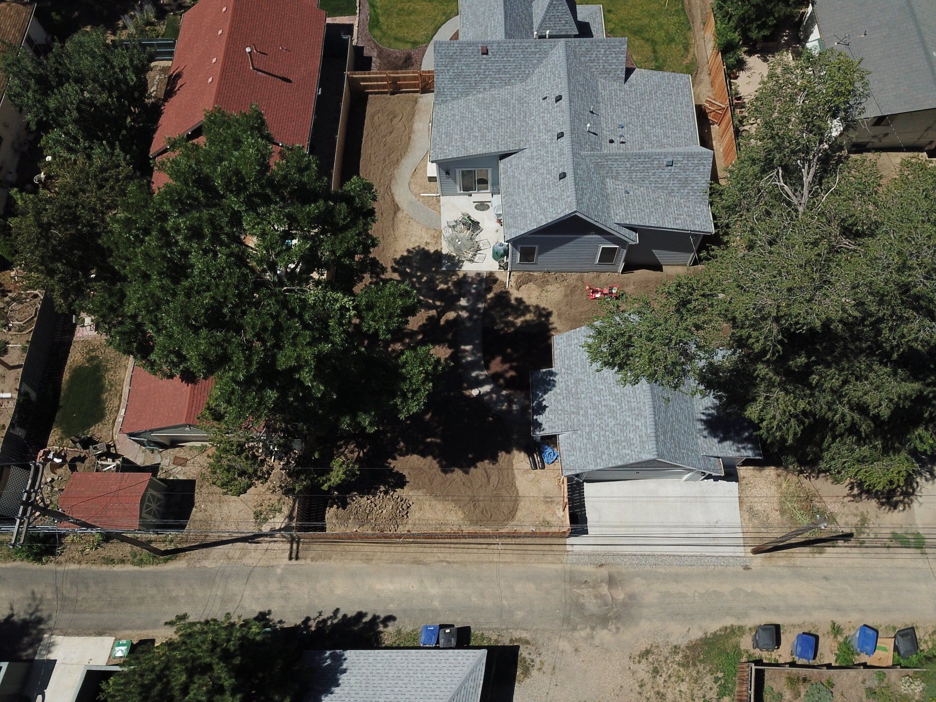 Aerial view of houses with gray and red roofs, trees, and a road.