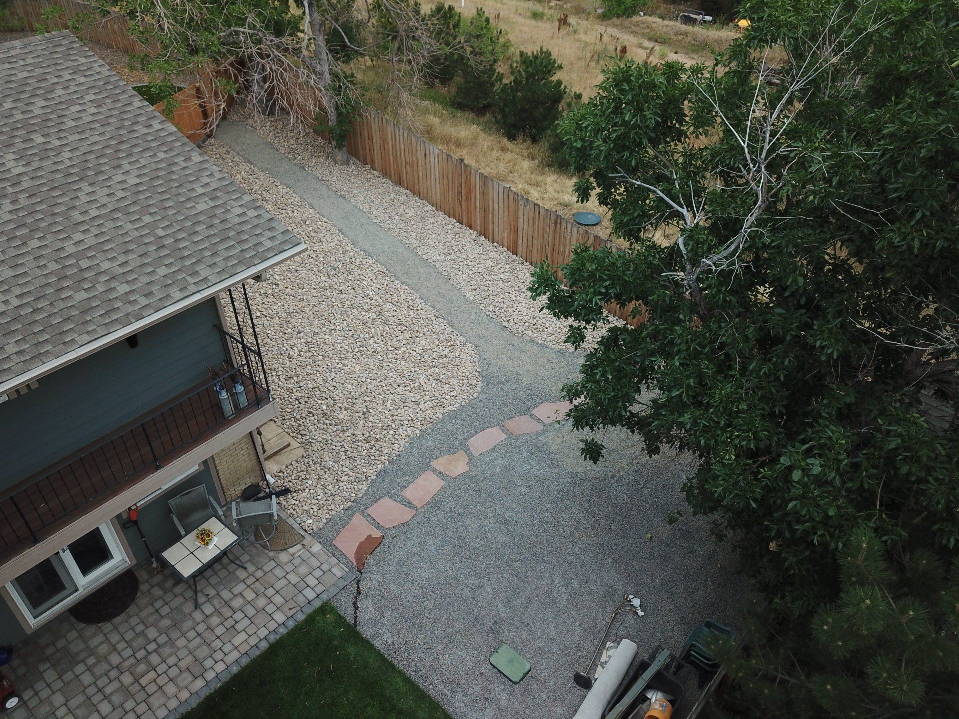 Aerial view of a backyard with a patio, gravel path, wooden fence, and a large tree.