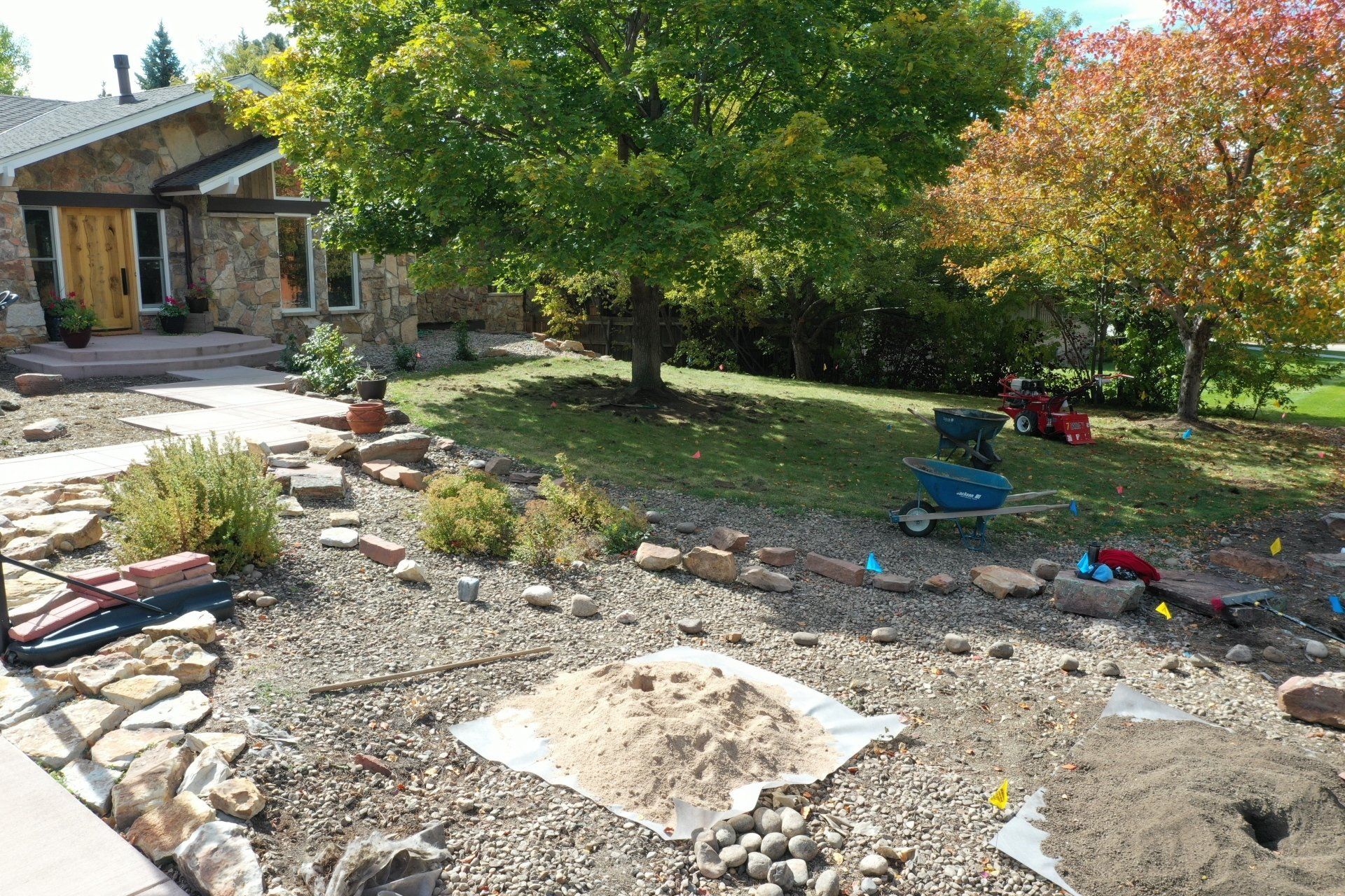 Front yard landscaping with rocks, plants, and a house with a stone facade under a sunny sky.