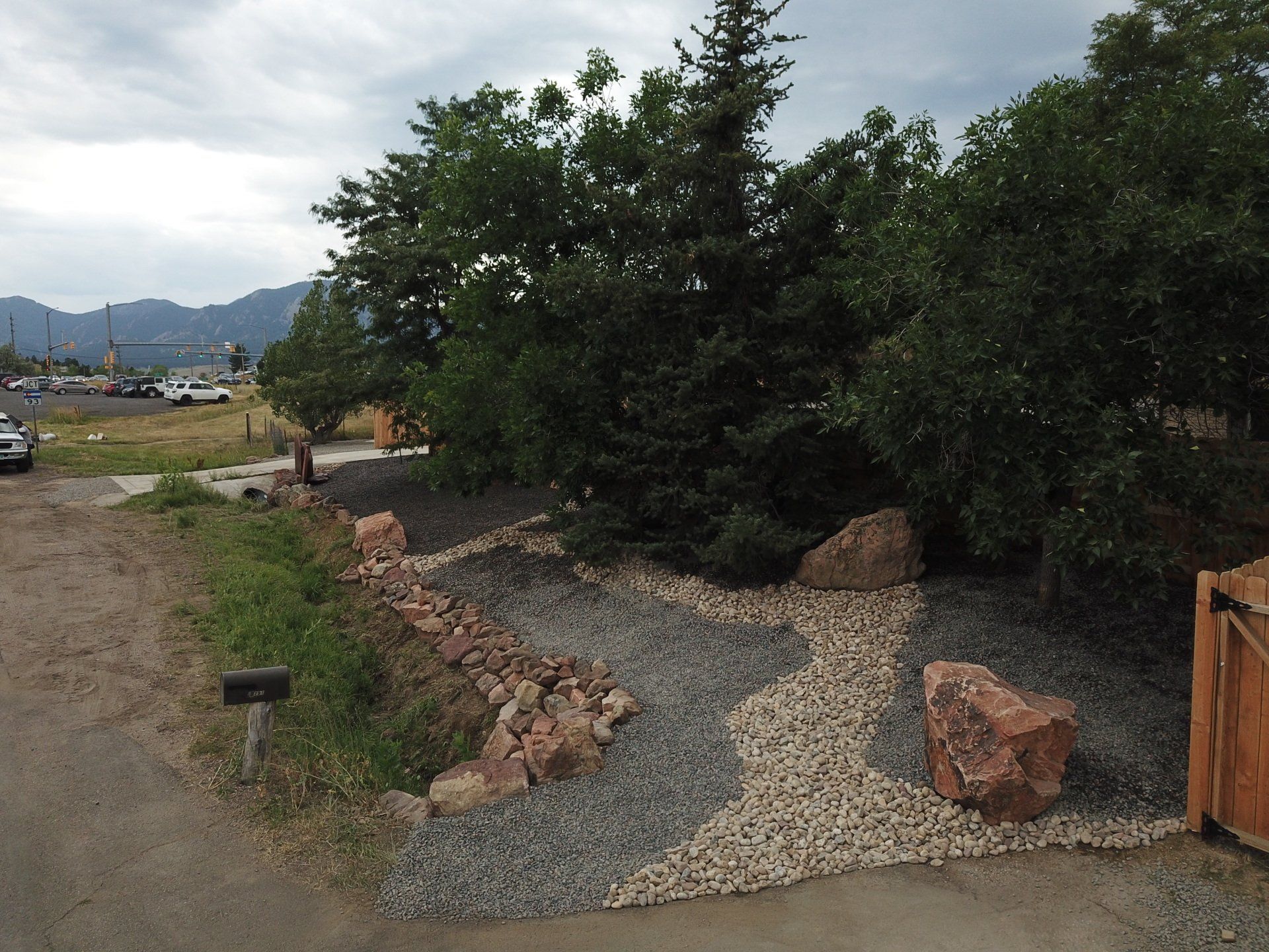 Landscaped yard with trees, rocks, and gravel near a road.