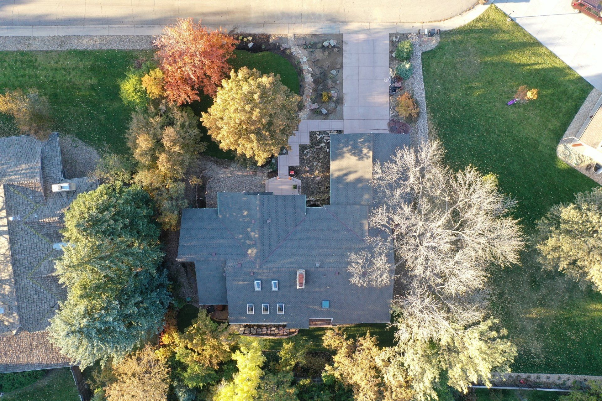 Overhead view of a house with a dark roof surrounded by colorful trees and a paved driveway.