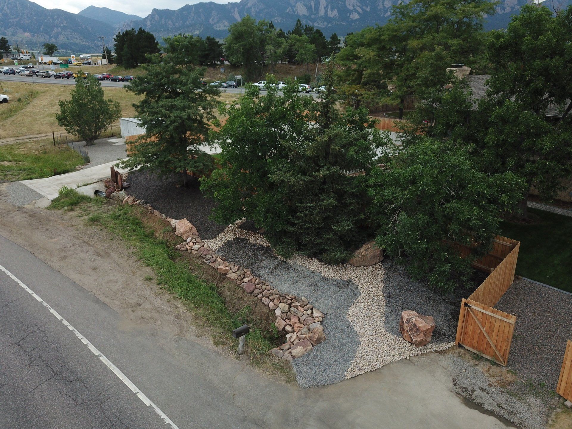 An aerial view of a yard with rock gardens, trees, a fence, and road with mountains in the background.