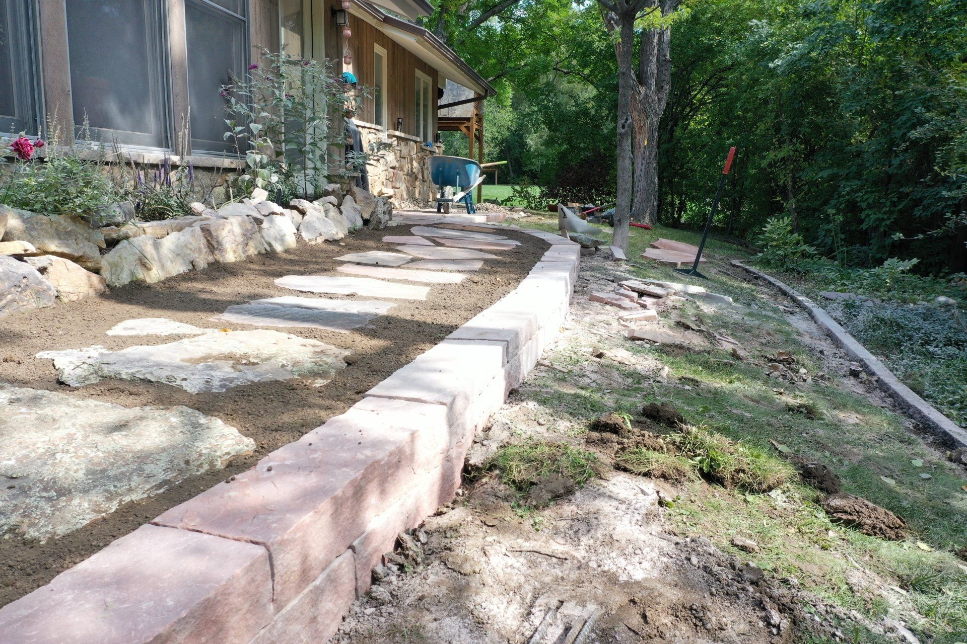 Stone pathway and brick retaining wall beside a house with a garden, outdoors.