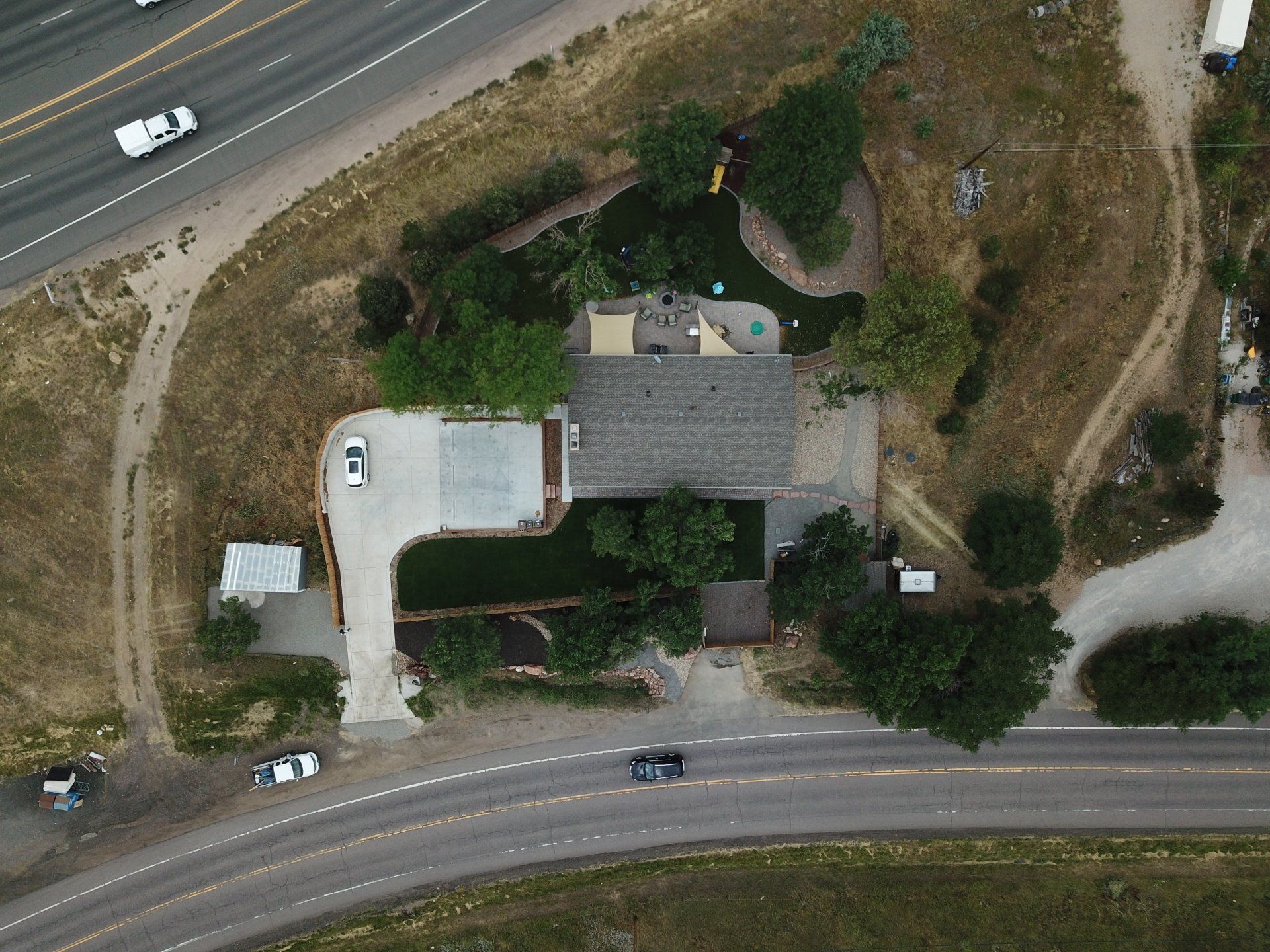 Aerial view of a house and property next to a highway. A car and trucks are visible on the road.