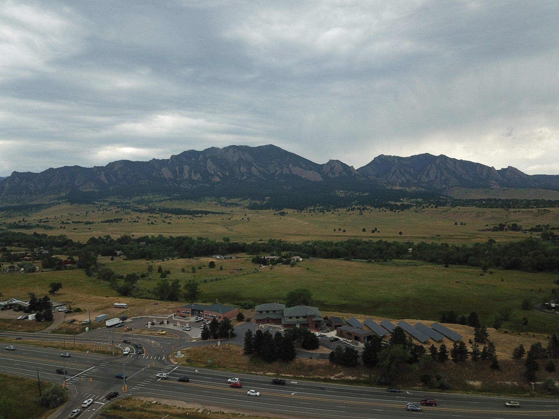 Mountain range over a valley, with buildings and a parking lot in the foreground under a cloudy sky.