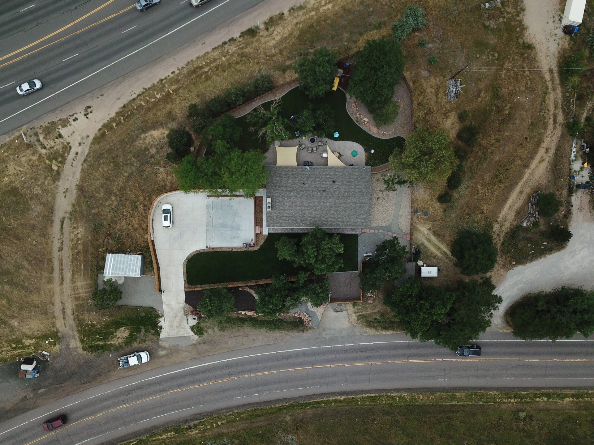 Aerial view of a house next to a road and highway, surrounded by trees and dry grass.