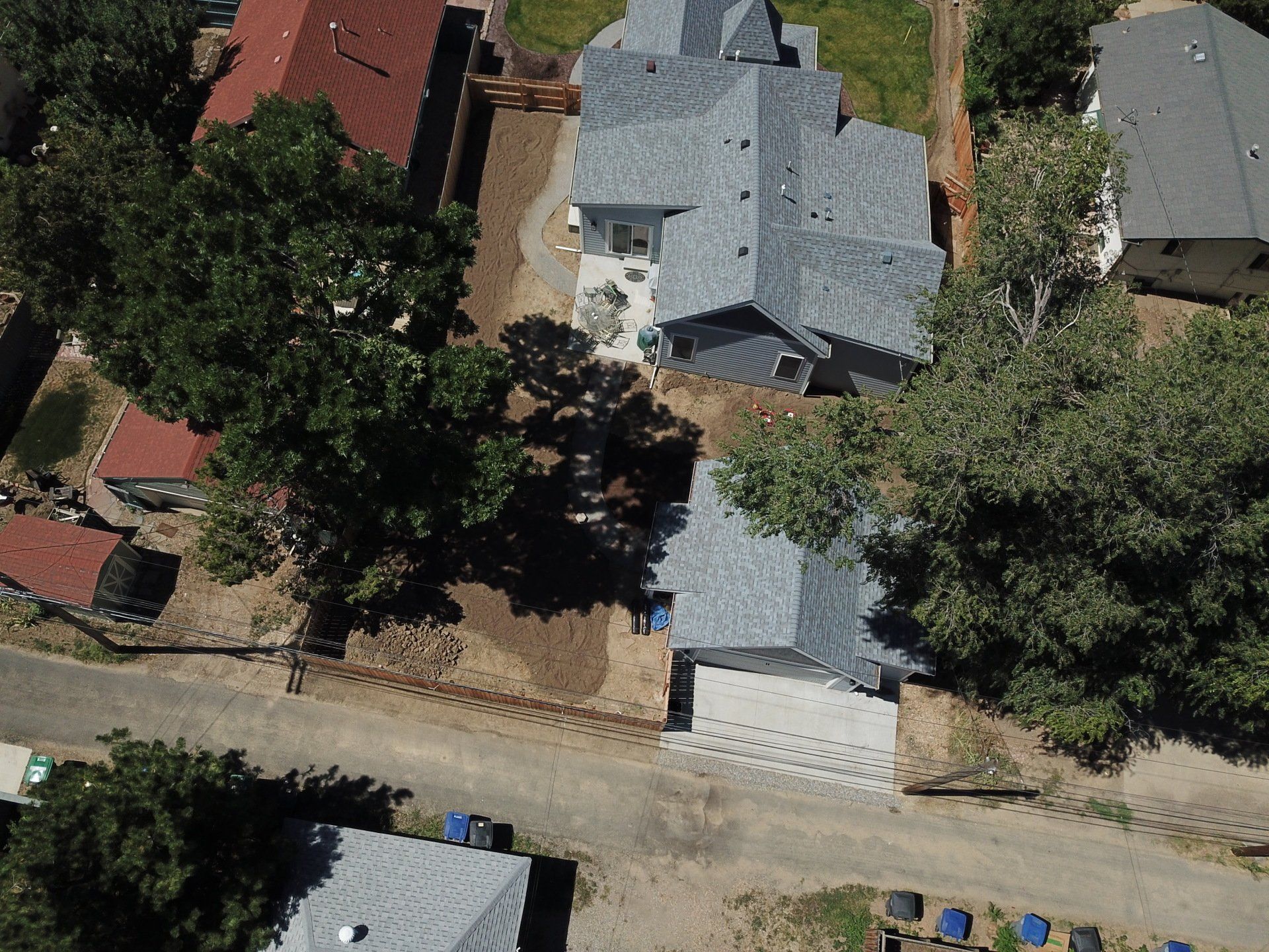 Aerial view of houses with gray roofs, trees, and a dirt road.