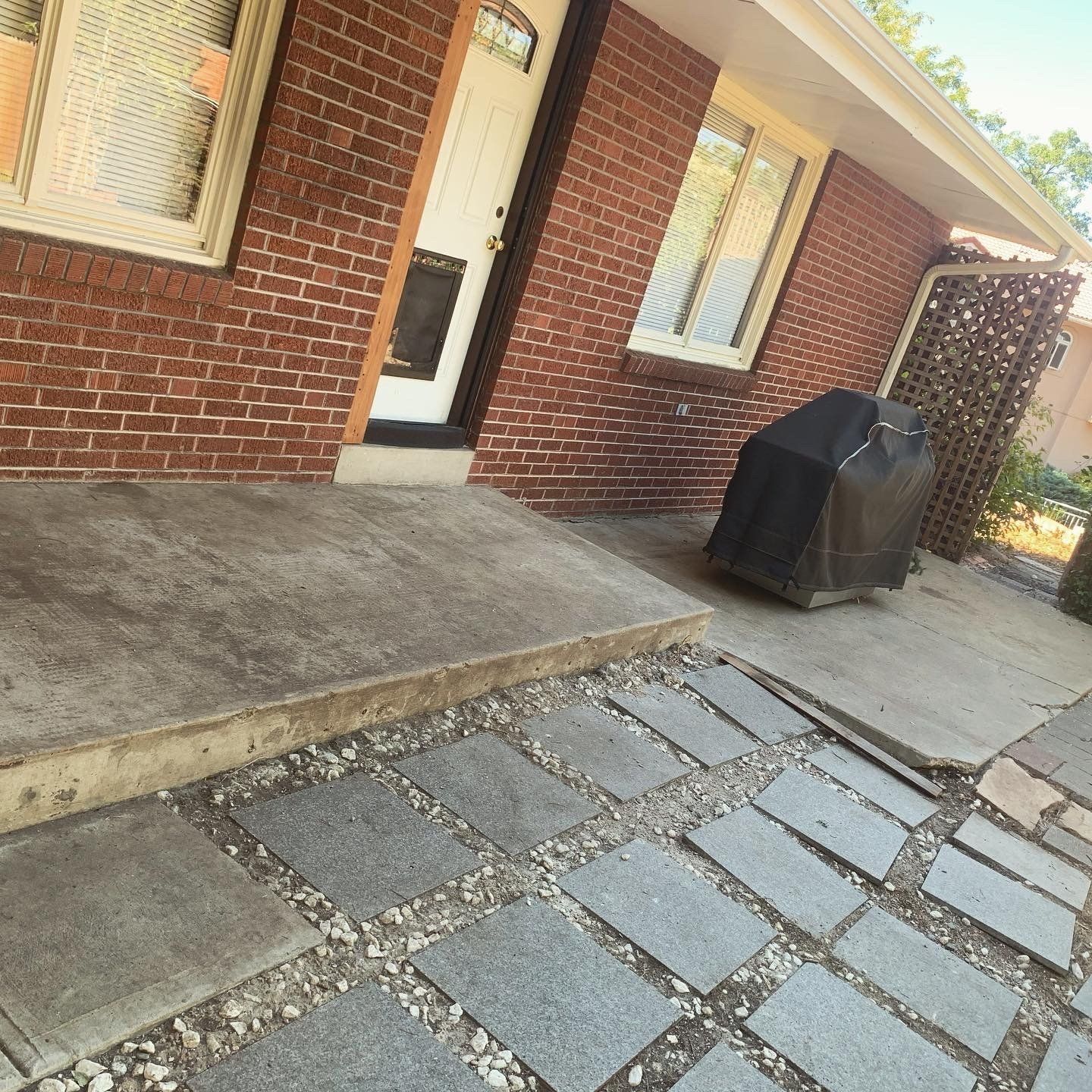 Brick house entrance with concrete step and walkway of stone squares, grill.