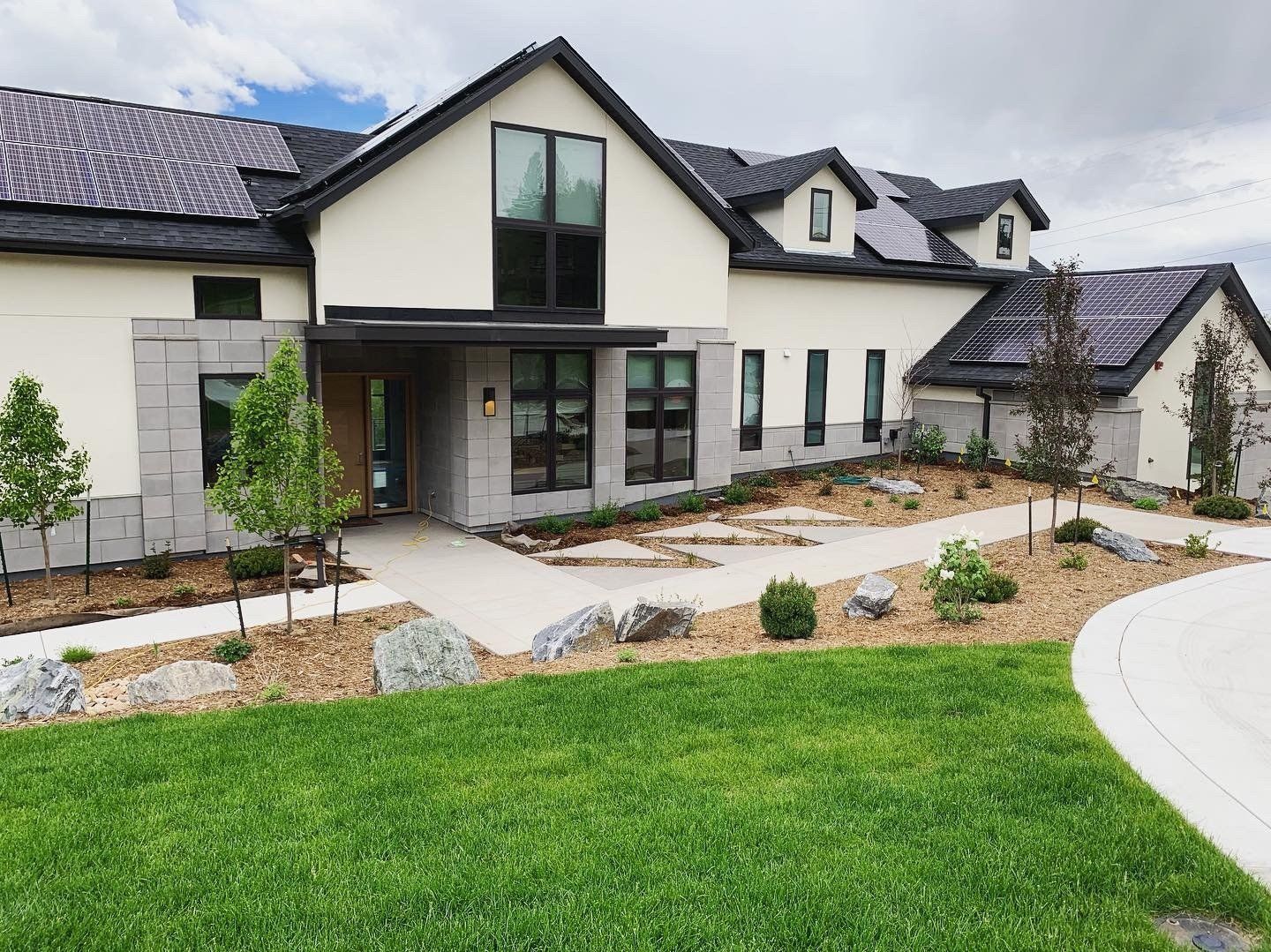 Modern beige house with a stone facade, solar panels, and landscaped yard.