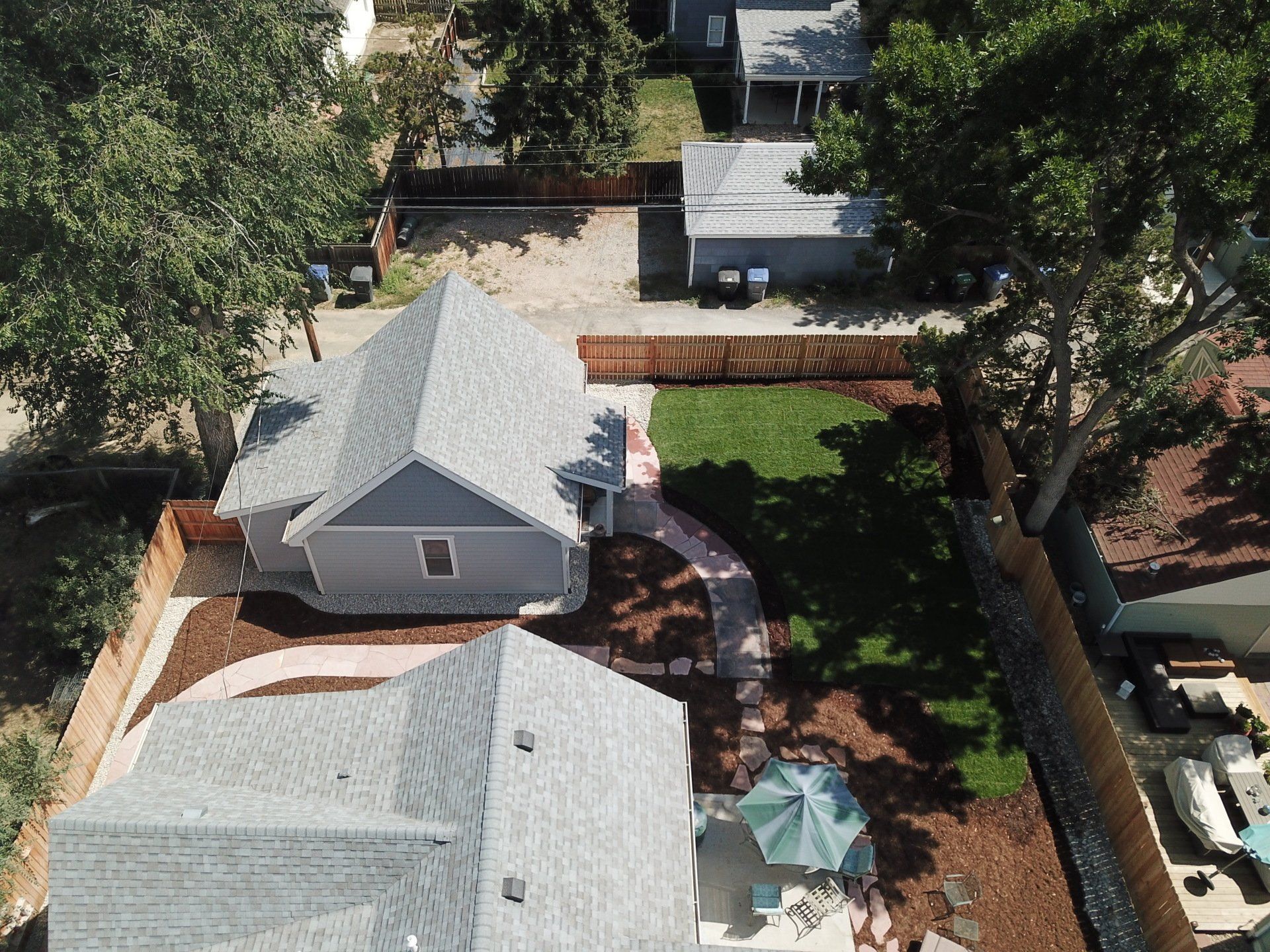 Aerial view of two houses with grey roofs, surrounded by landscaping, lawn, and fencing.