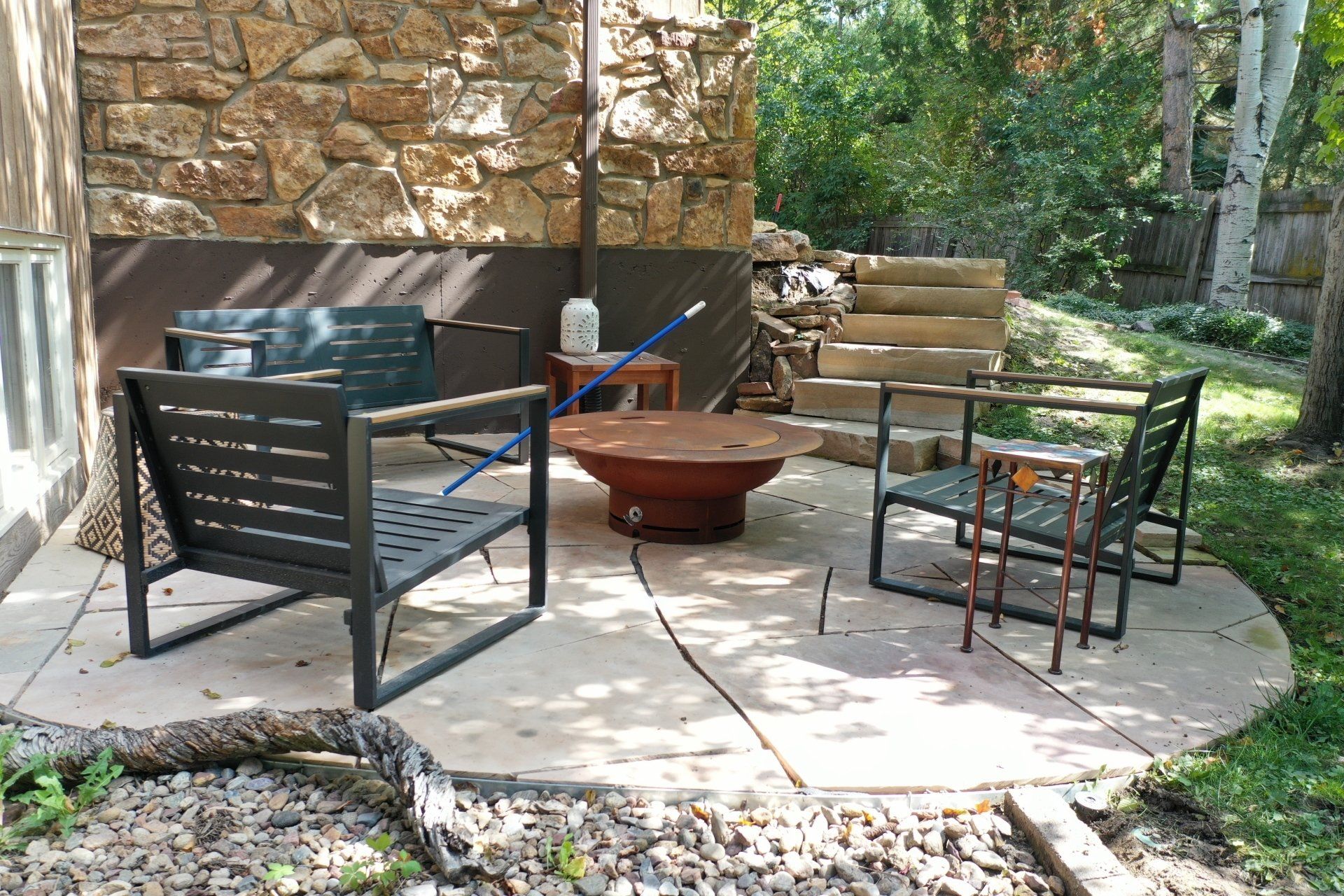 Patio with seating around a fire pit next to a stone wall and some steps.