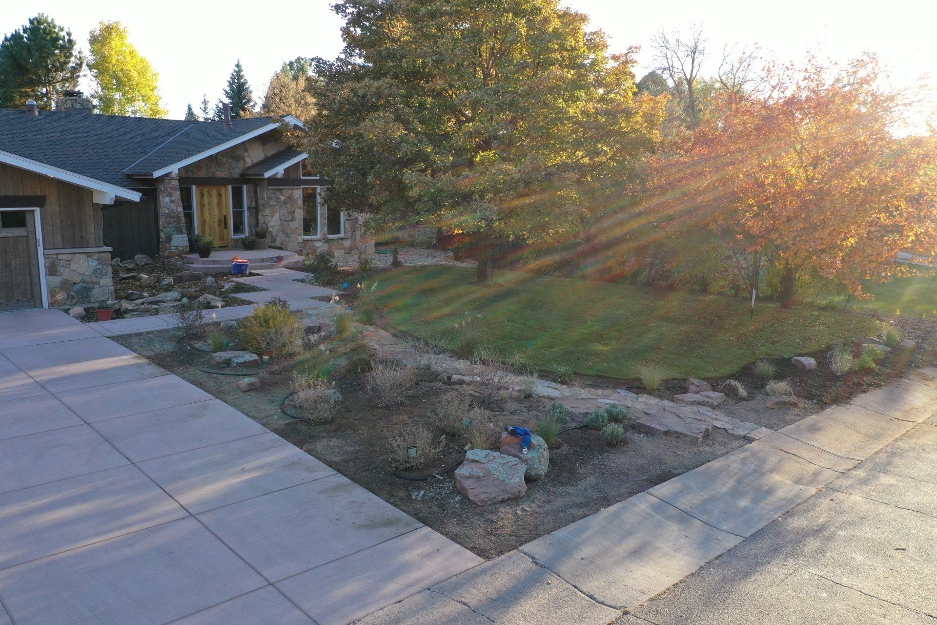 House exterior with a stone facade, driveway, landscaping, and sunlight.