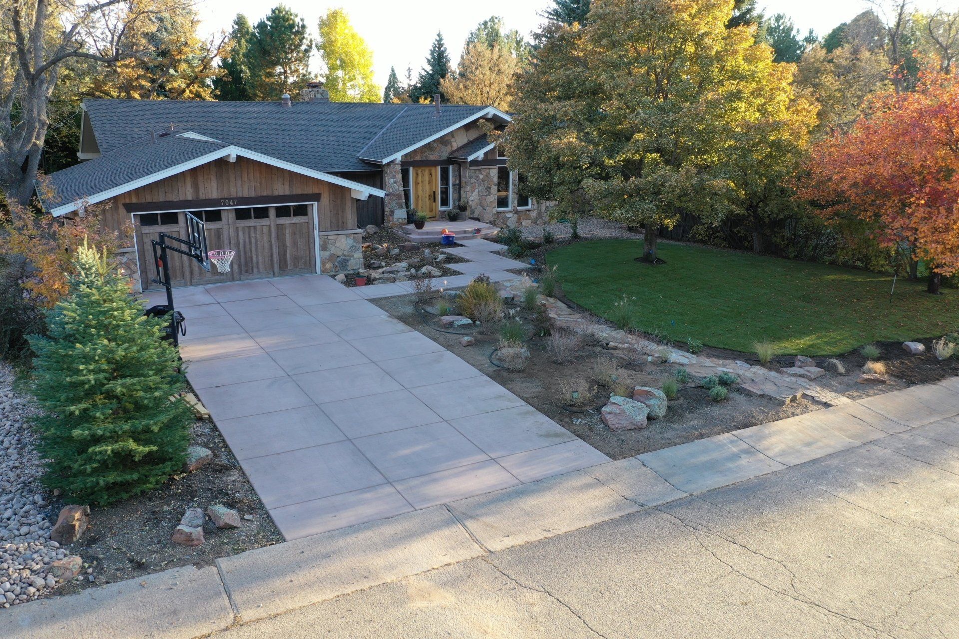House with stone and wood exterior, driveway, landscaped yard, and basketball hoop.