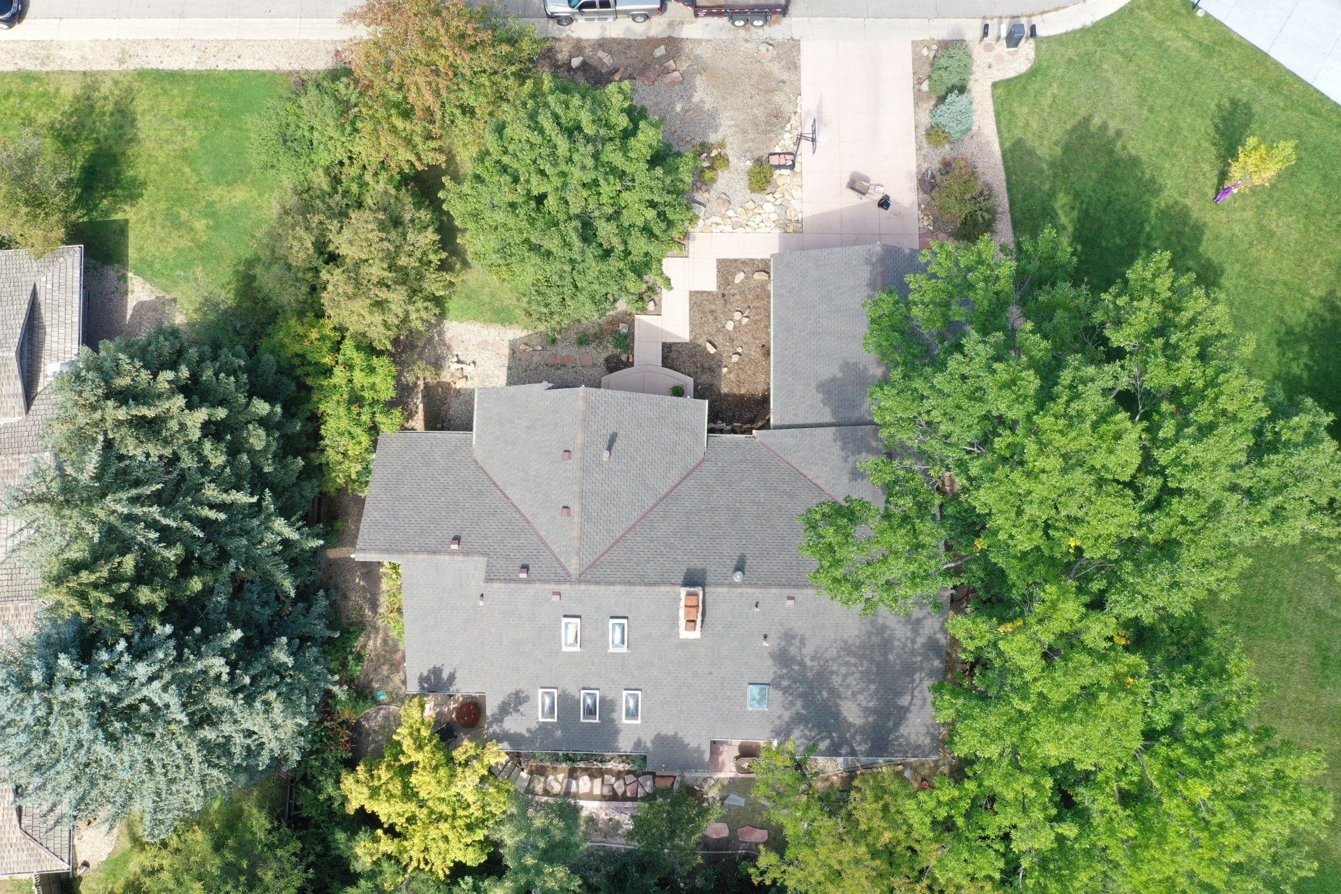 Overhead view of a house with a dark roof surrounded by trees and a pathway.