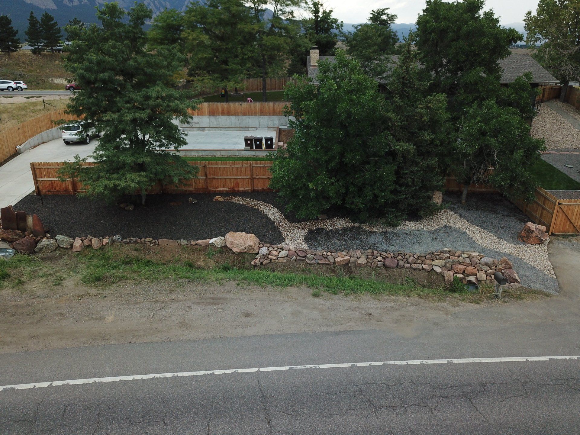 A house with a landscaped yard and trees behind a road, mountains in the distance.