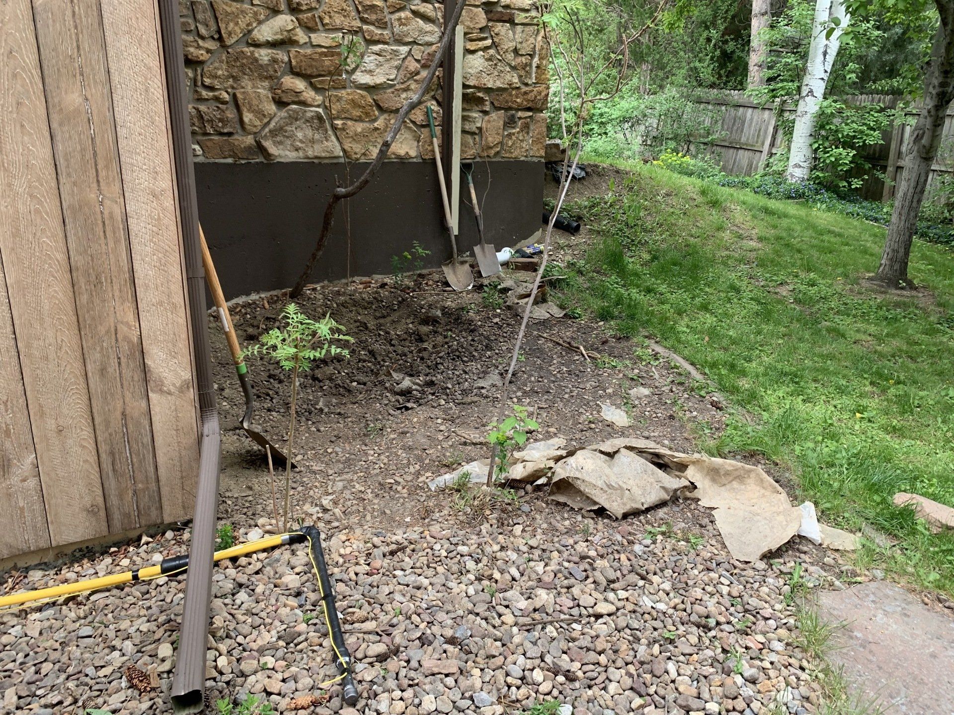 A small garden bed with rocky ground next to a wood and stone building exterior.