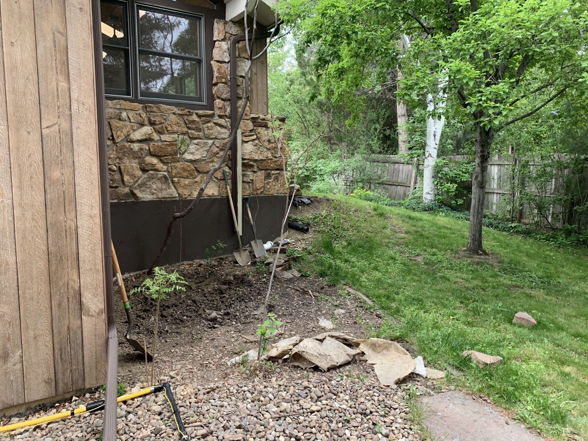 Side of stone building with exposed foundation, dirt, gravel, and grass.