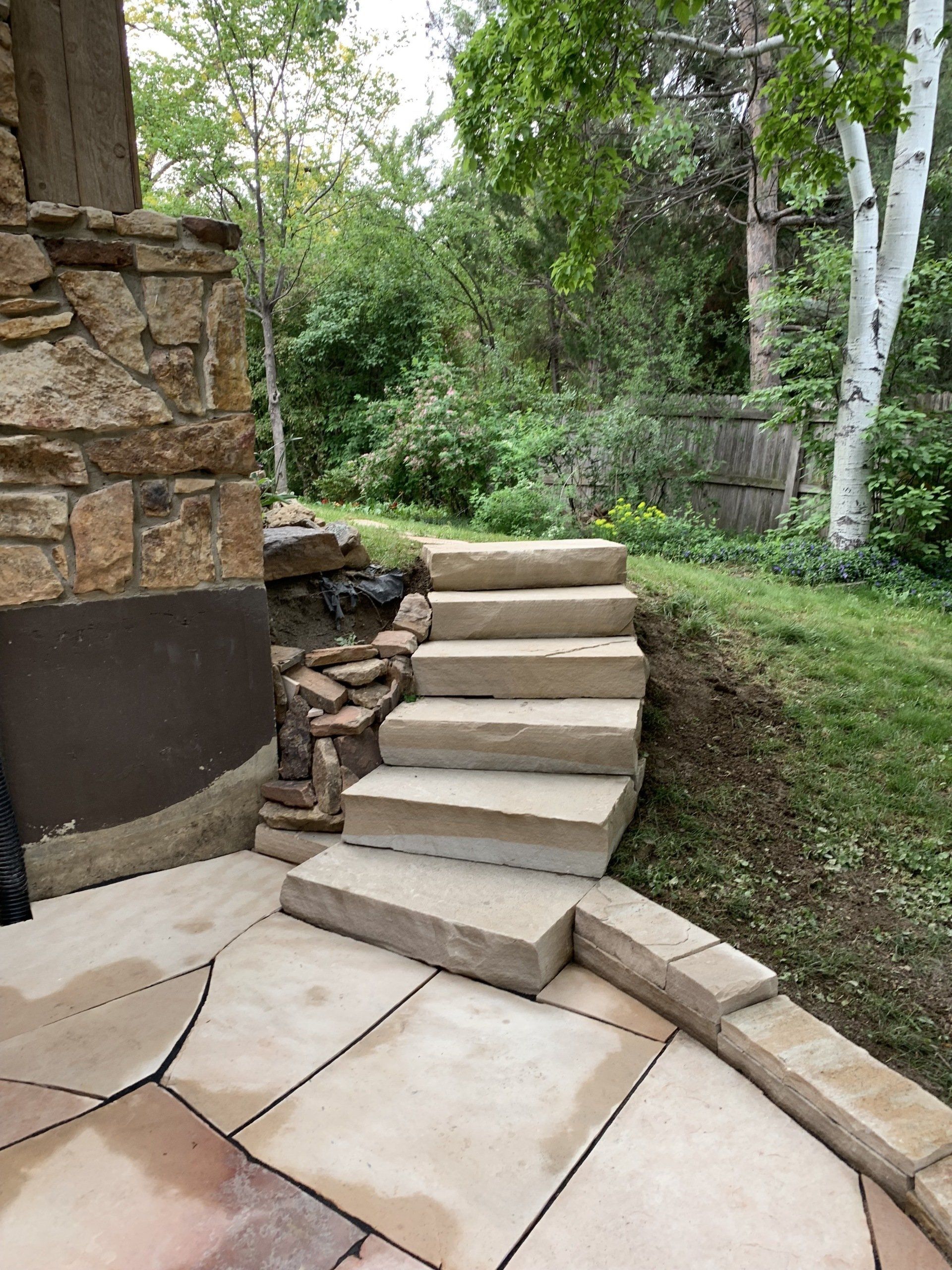 Stone steps leading up to a grassy area, next to a building and trees.