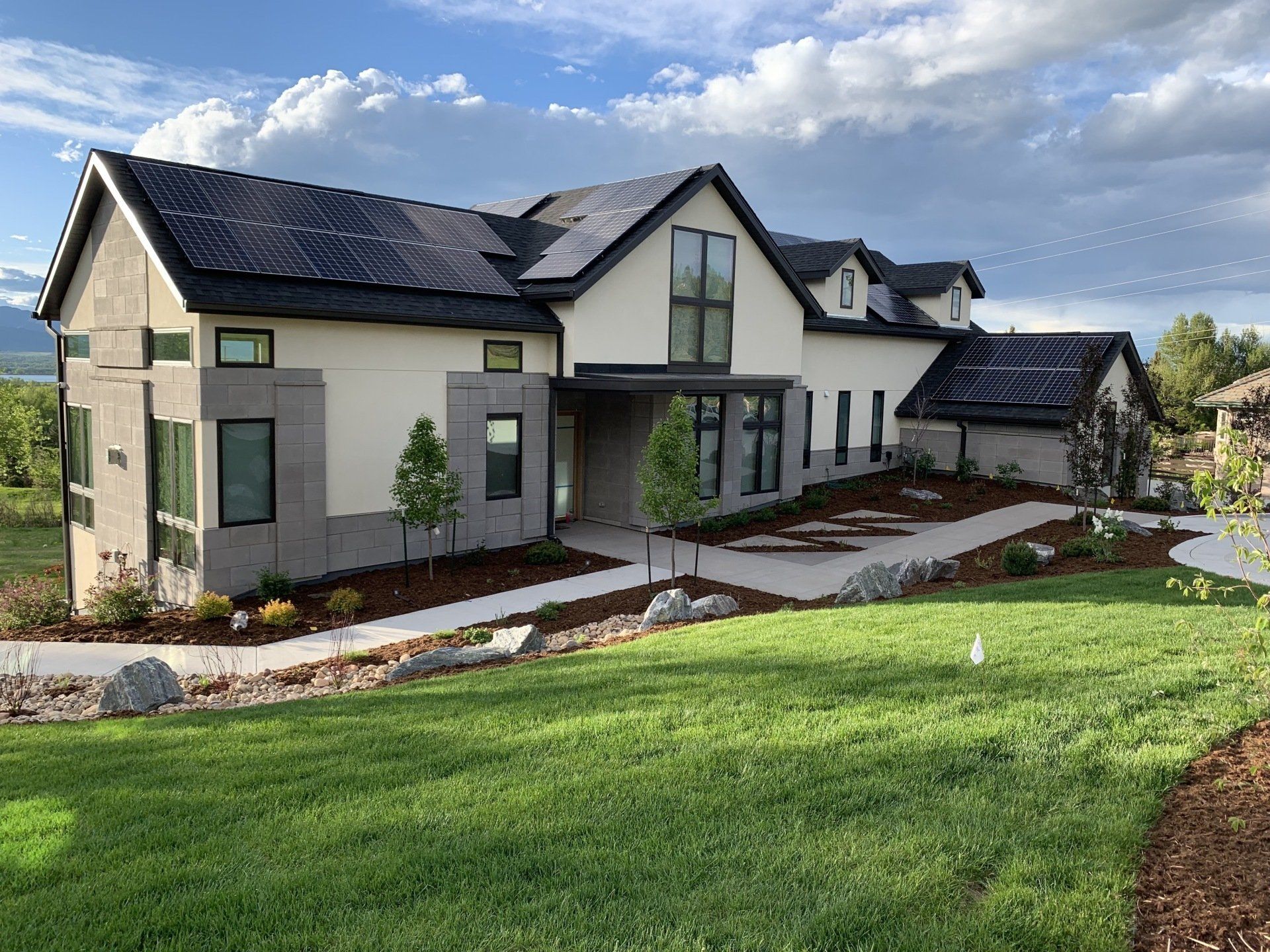 Modern home with dark roof, tan and gray exterior, lush green lawn, and mountain backdrop.