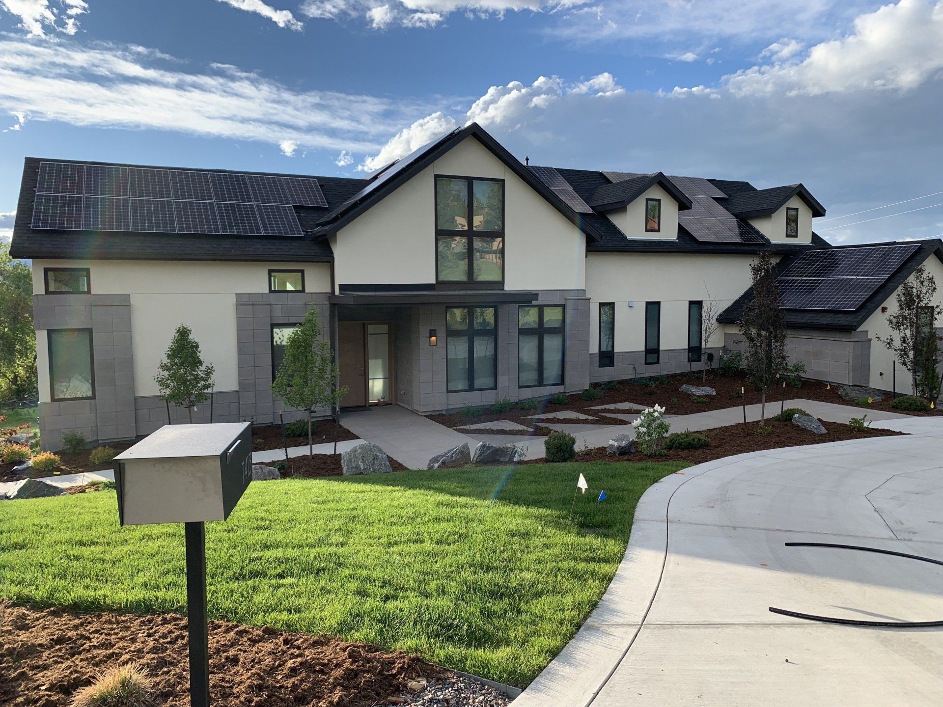 Modern house with light-colored walls, black trim, and a curved driveway under a cloudy sky.