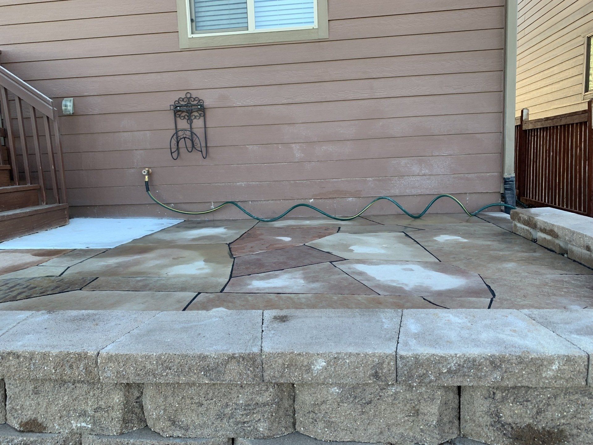Patio with stone pavers, retaining wall, house siding, and a garden hose.