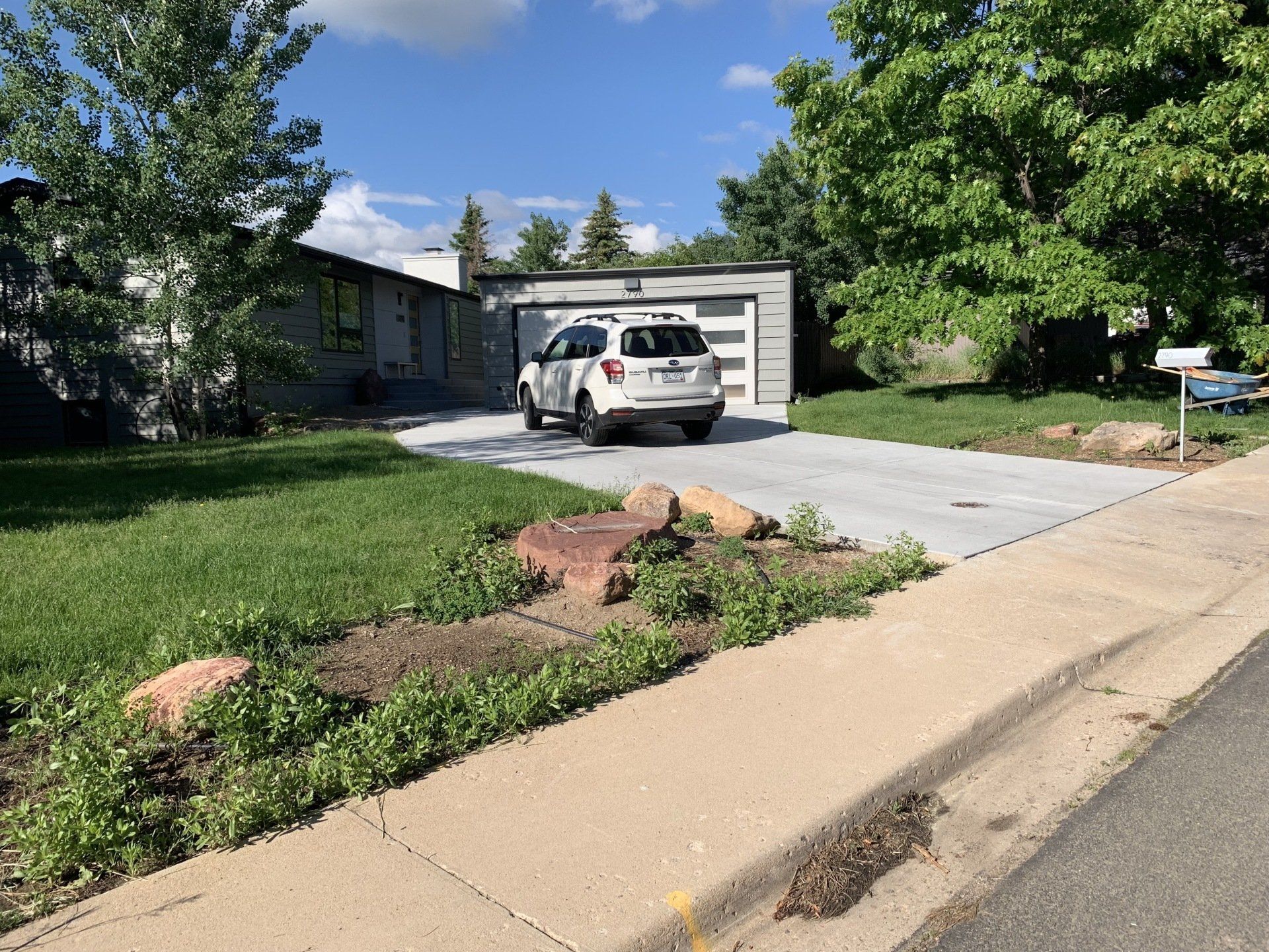 A white SUV parked in a driveway in front of a gray garage and house with grass and trees.