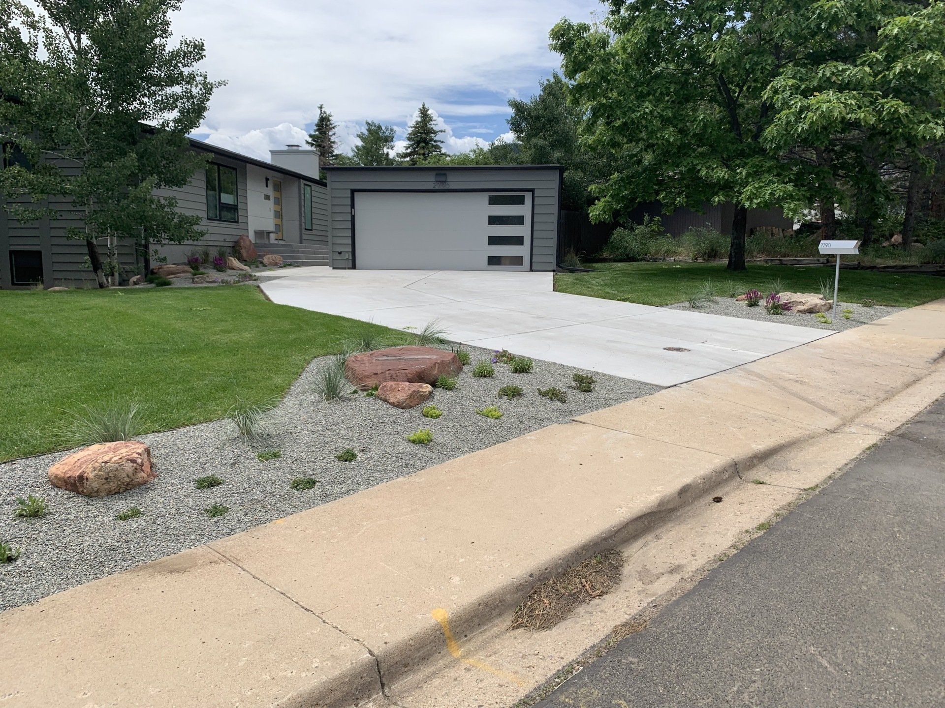 House exterior with gray garage, driveway, green lawn, landscaping with rocks, and a mailbox.