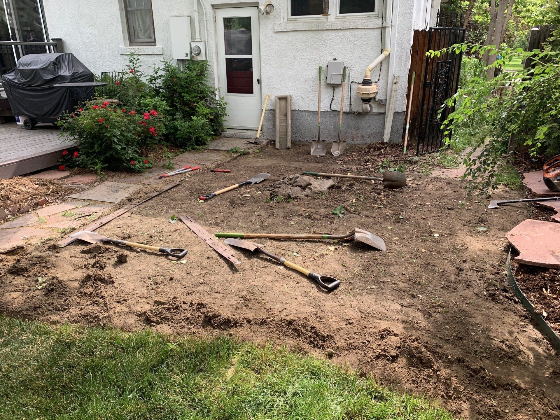Backyard dirt area with gardening tools and house in the background.