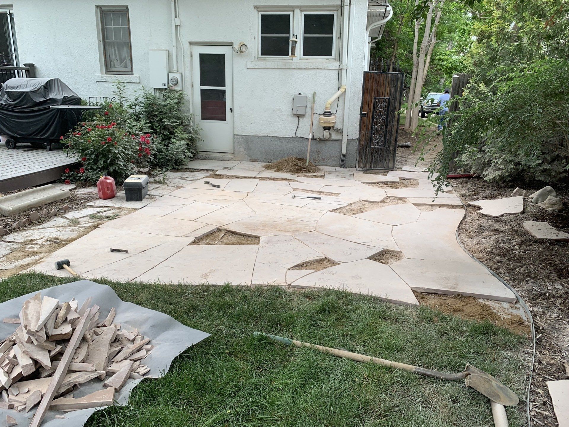 Backyard patio with broken concrete slabs, dirt, and tools.