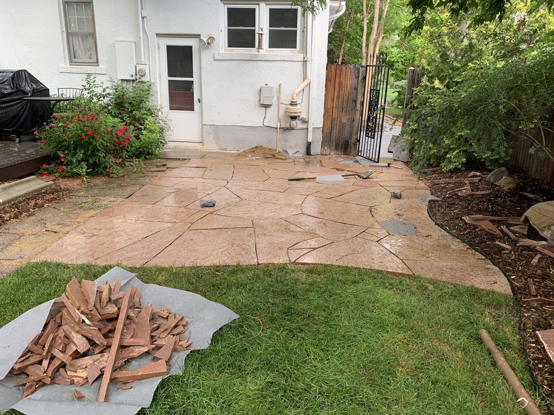 Backyard patio with flagstones, grass, and a door to a white house.
