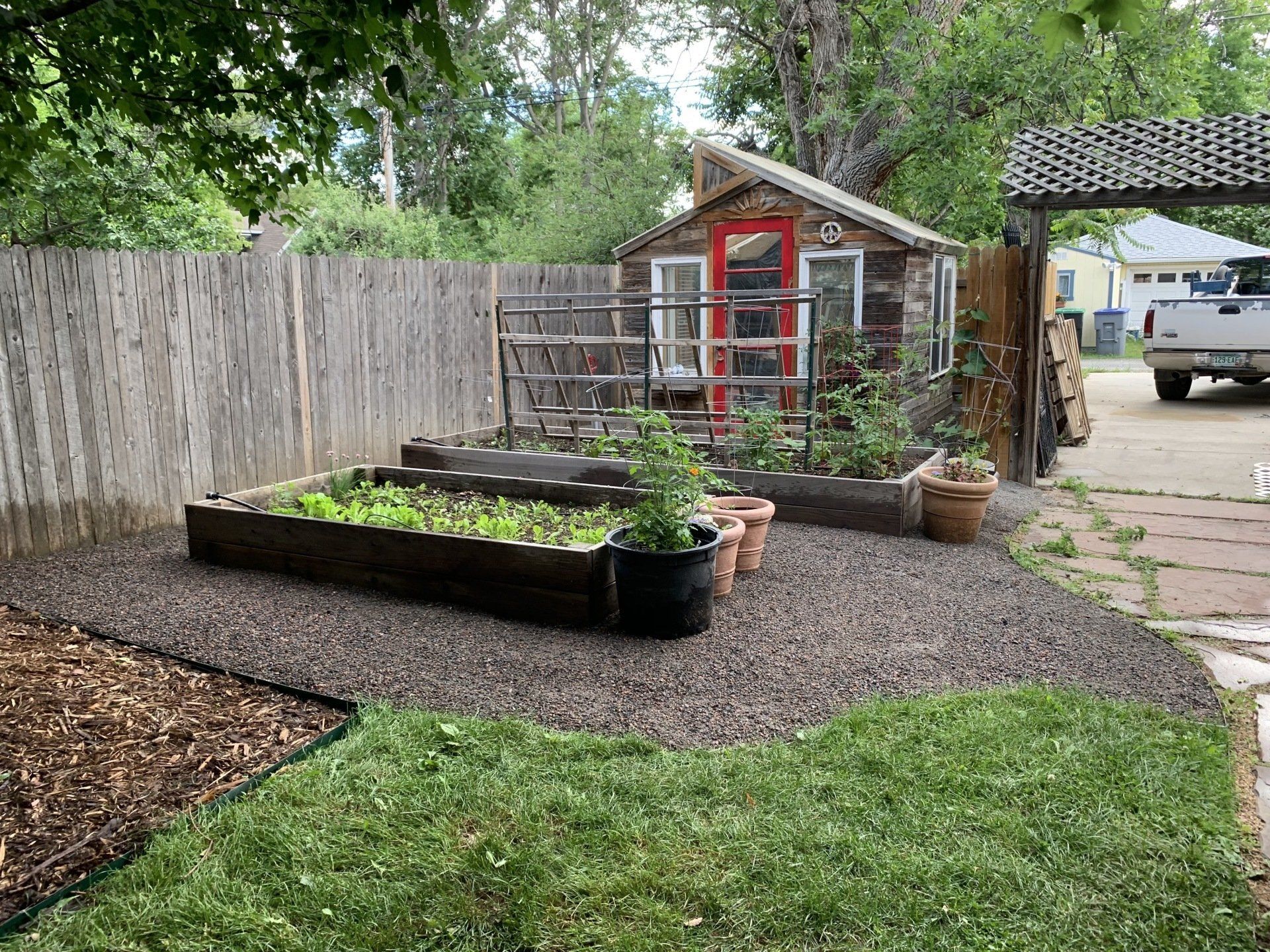 Backyard garden with raised beds, shed with red door, gravel path, and wooden fence.