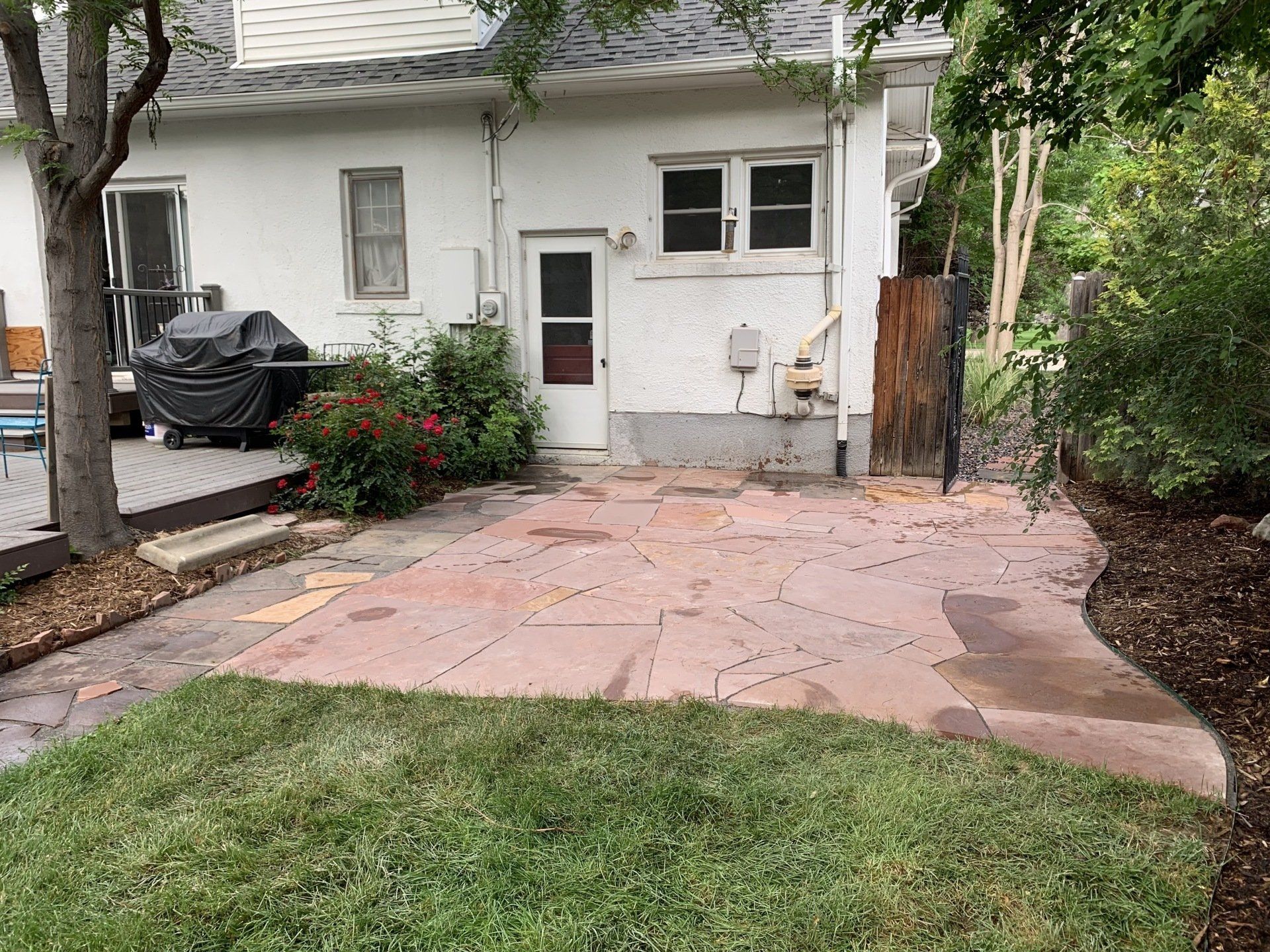 Backyard patio with flagstone, grass, and a white house.