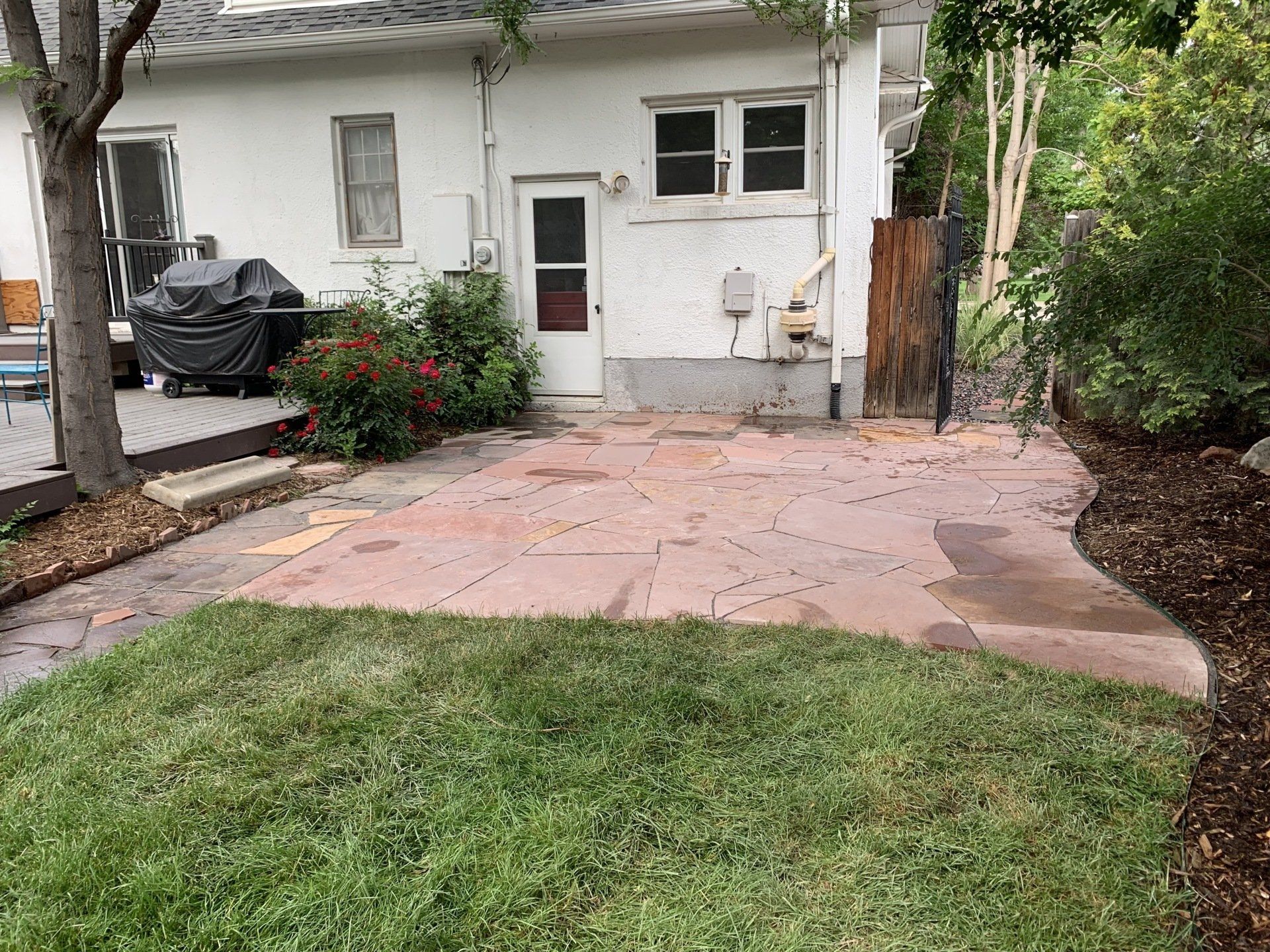 Backyard patio with red stone pavers, small lawn, and white house.