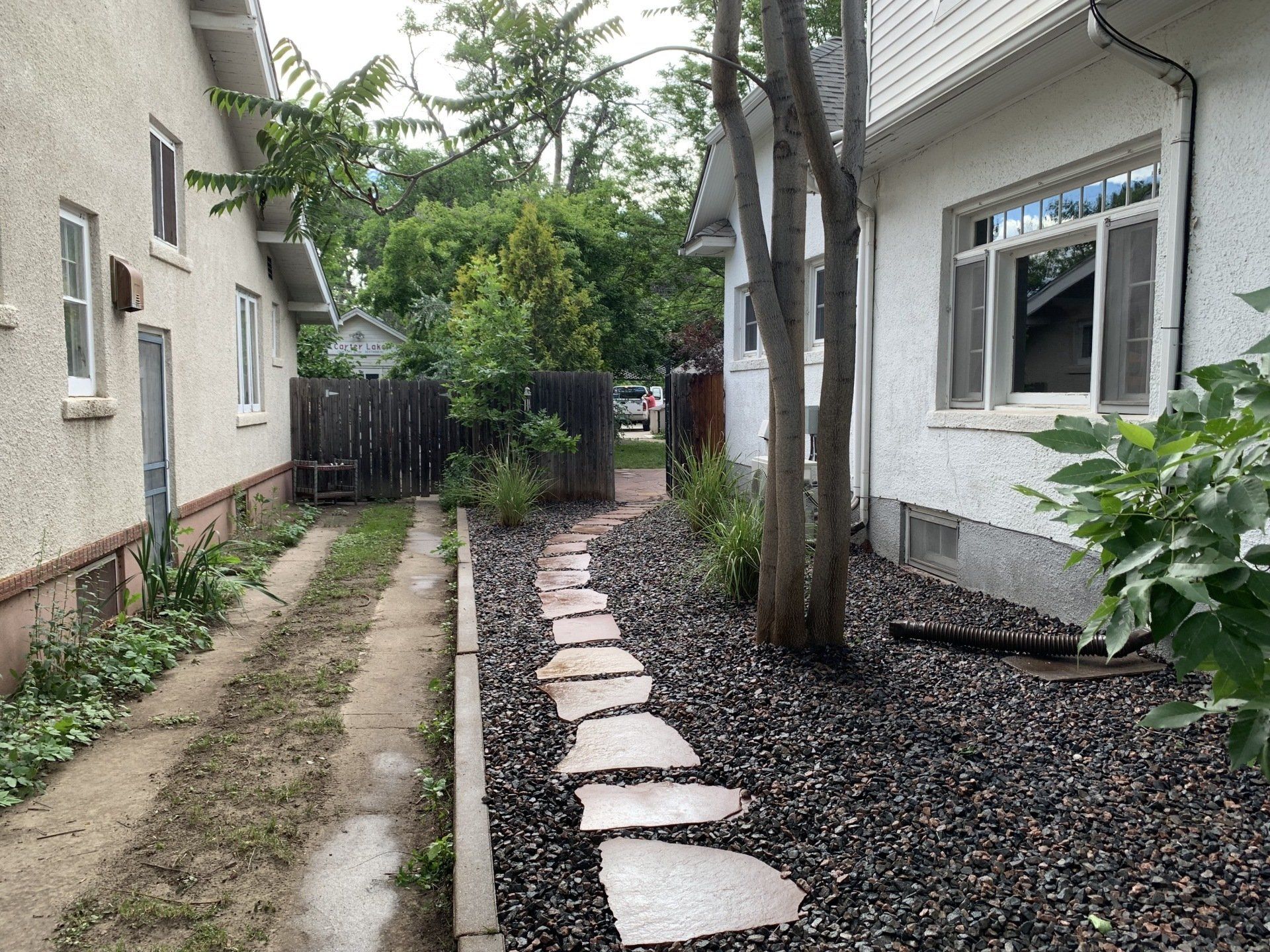 Stone path between two houses, leading to a wooden fence. Gravel and plants flank the path.