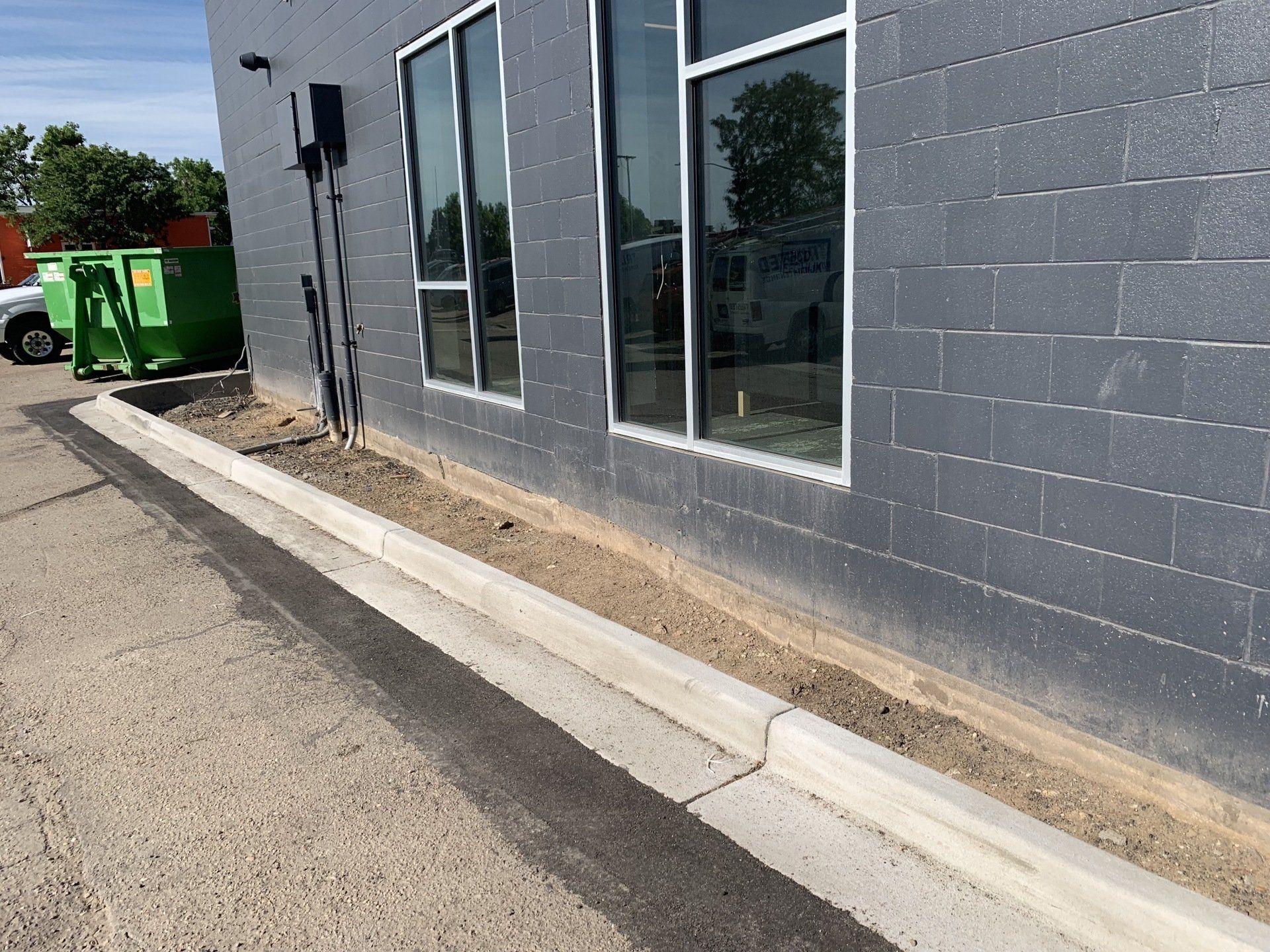 Gray building with windows, concrete curb, asphalt, and dirt strip.