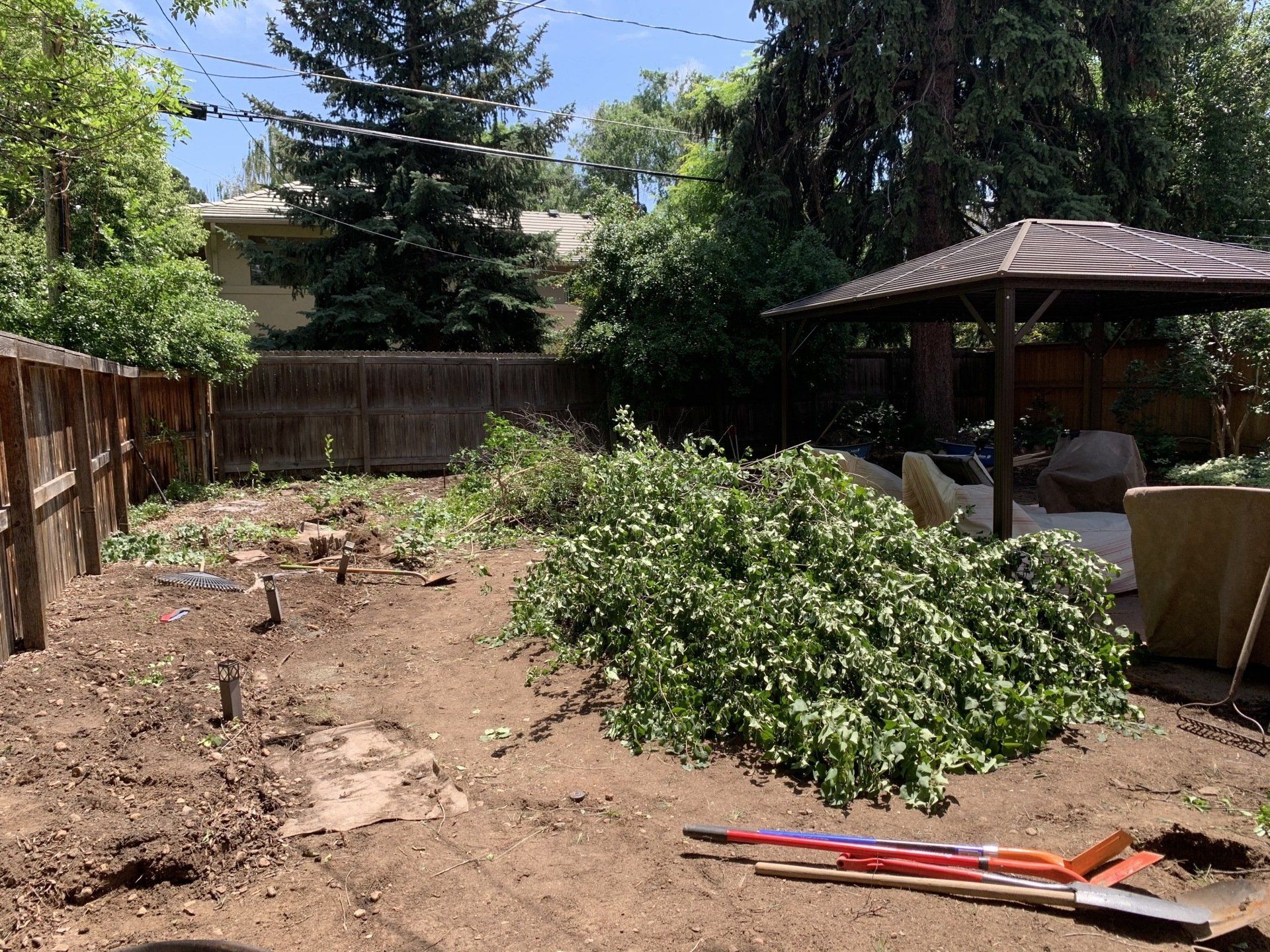 Backyard after landscaping with piles of green cuttings, dirt, fence, gazebo.