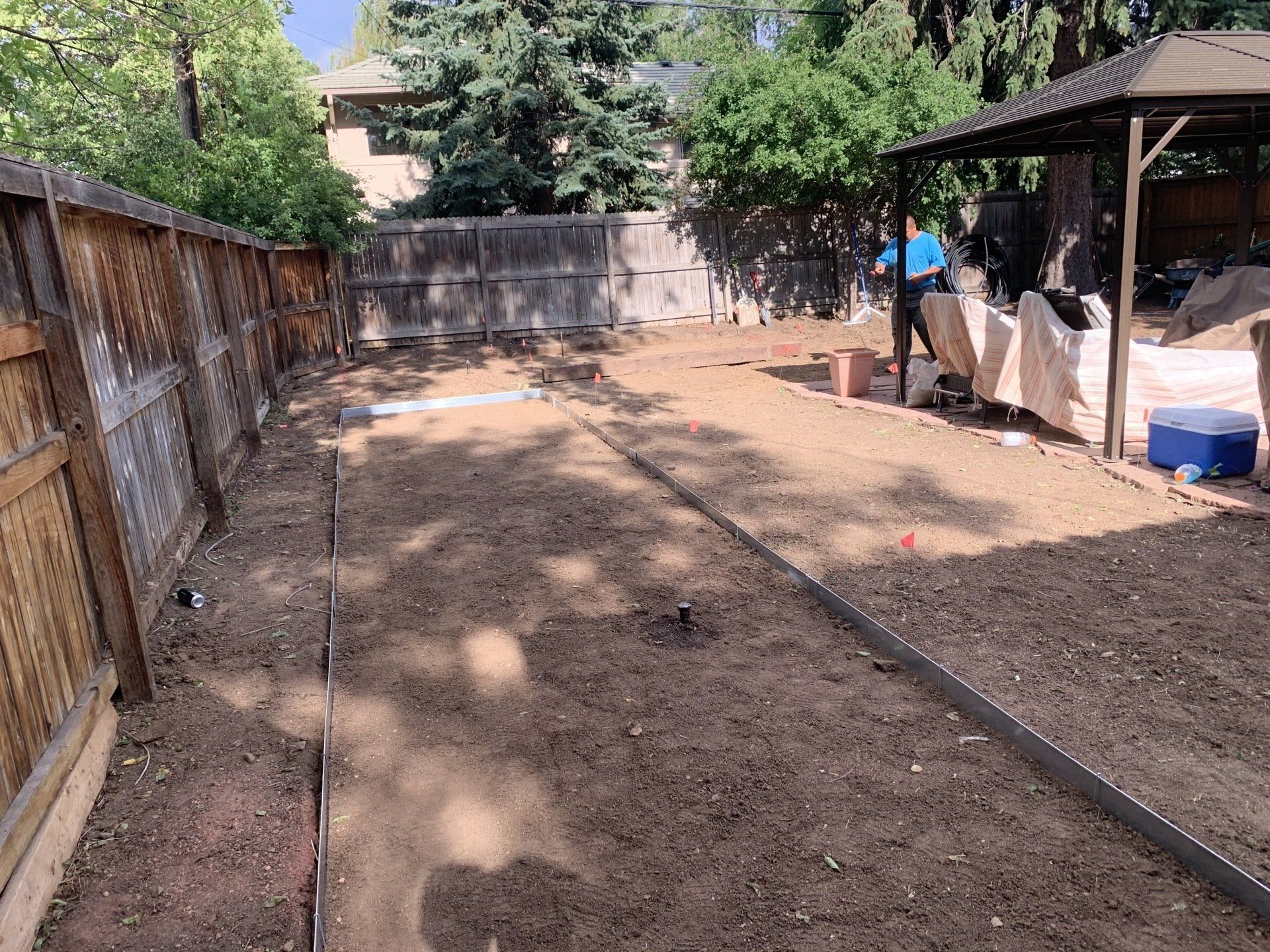 Backyard with dirt ground, wooden fences, gazebo, and some construction materials.