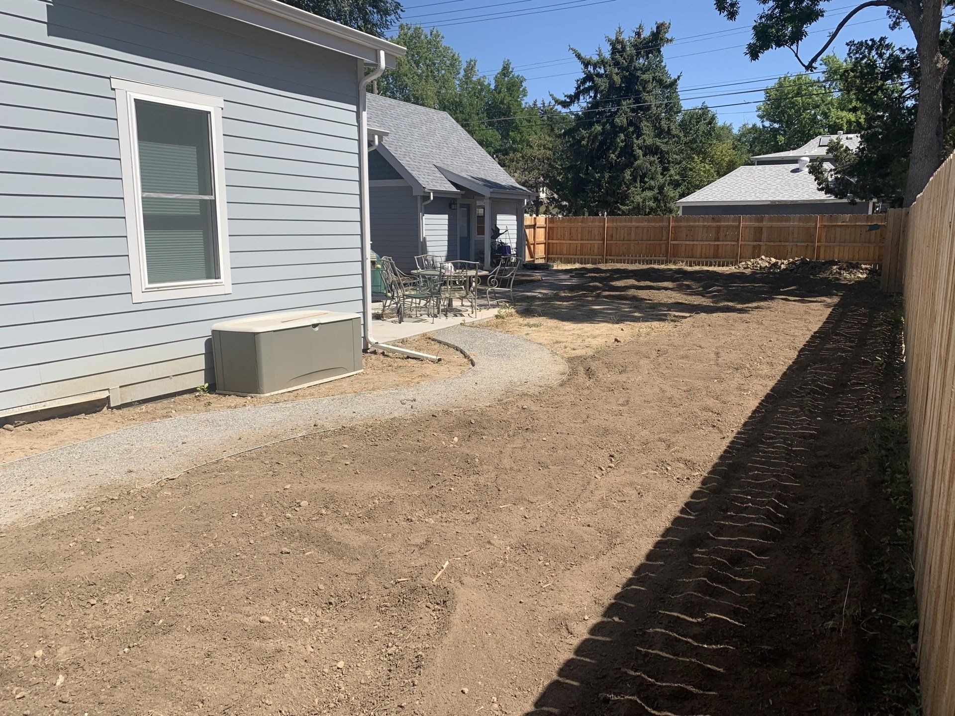 Side view of a house and yard with gravel path, bare earth, and a wooden fence.