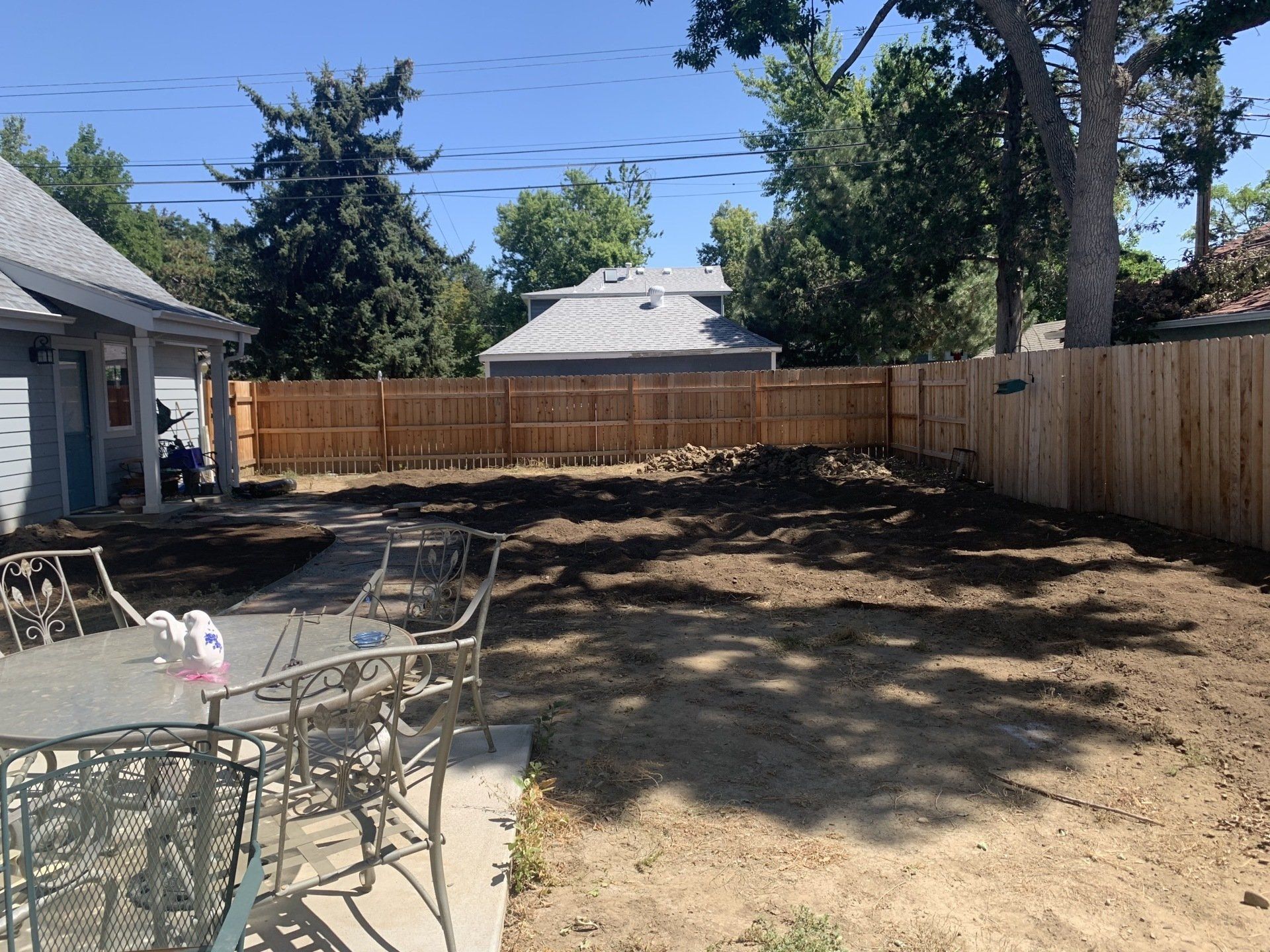 Backyard with new fence, dirt patch, patio furniture, and house.