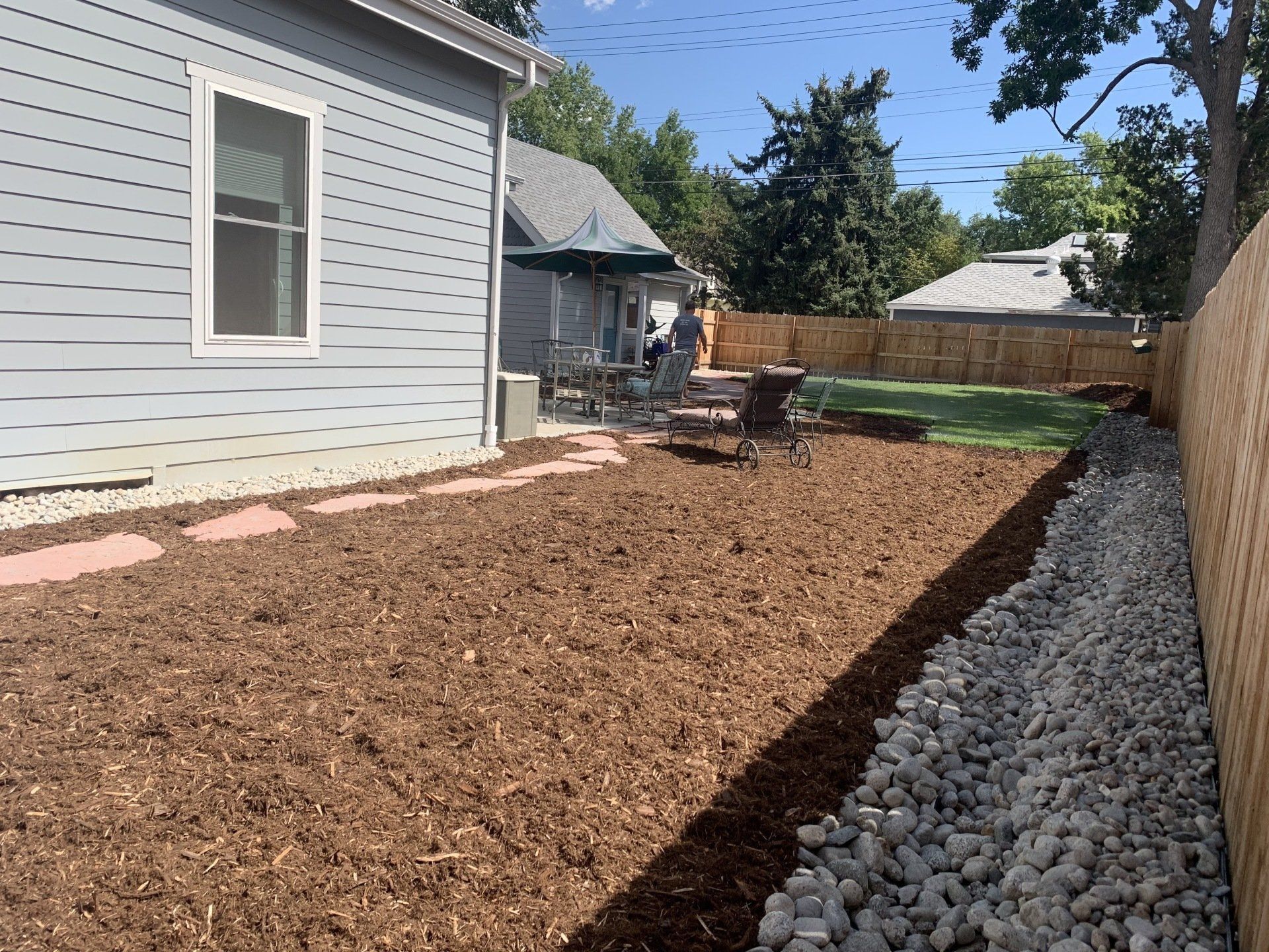 Backyard with wood mulch, stone border, and wooden fence.