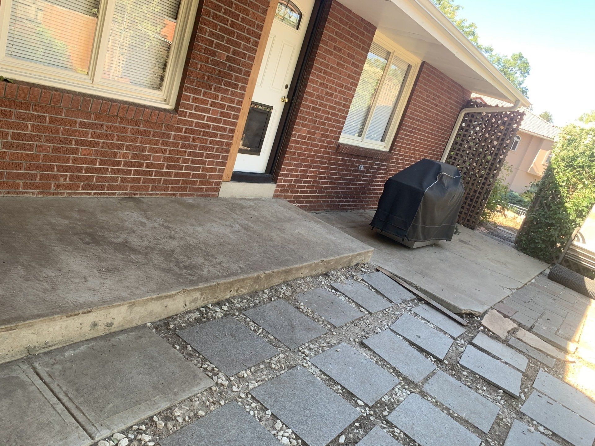 Brick house exterior with concrete steps and flagstone walkway. A grill is visible near the entrance.