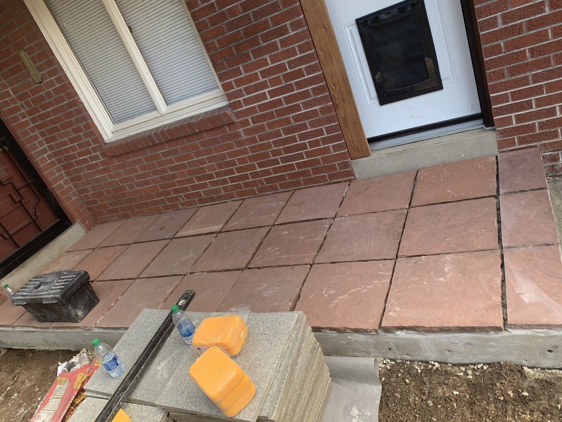 Red brick house entrance with new reddish tiles being installed. Construction tools and materials visible.