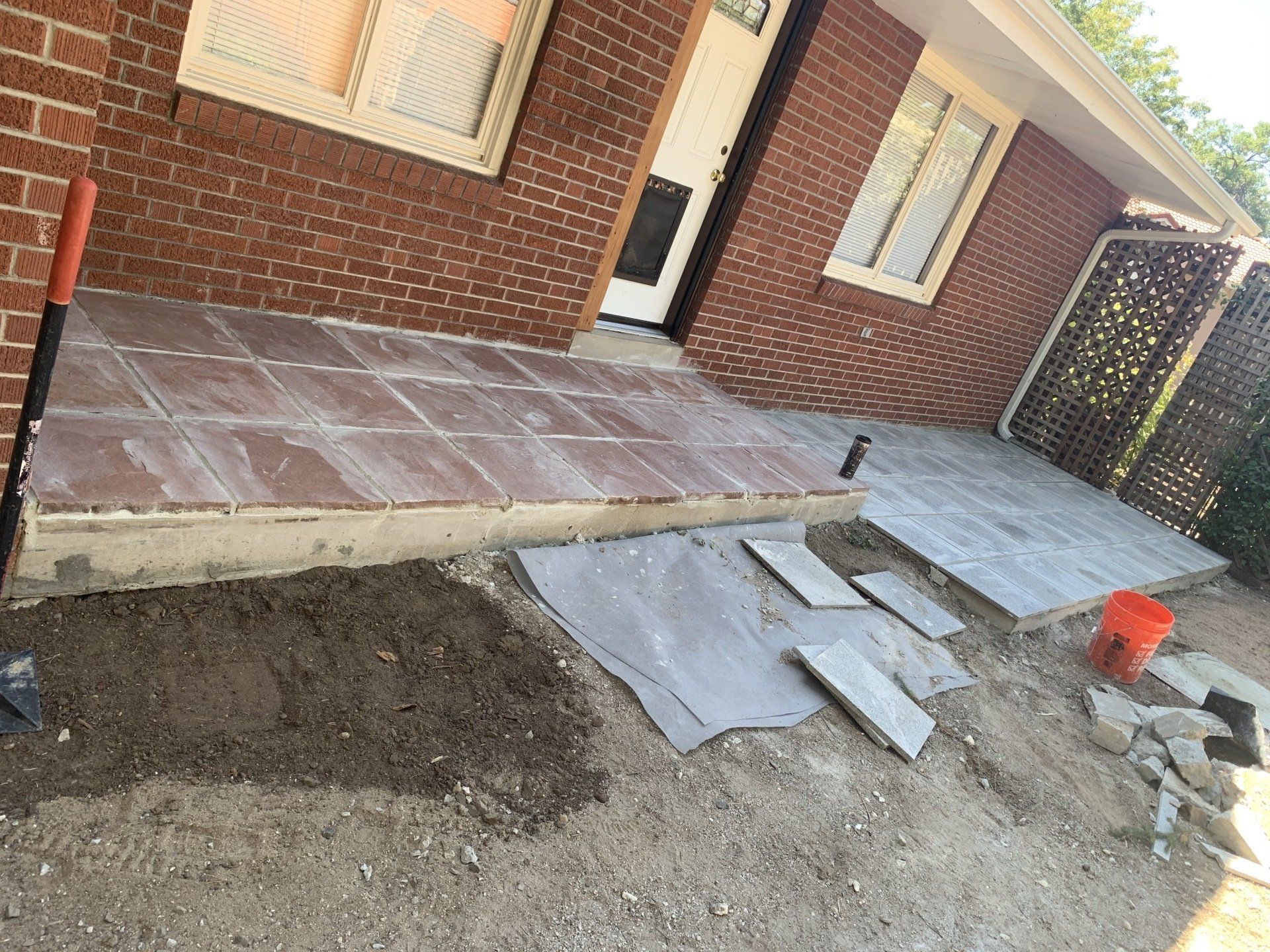 Brick home with a tiled porch under construction; materials, shovel, and dirt present.