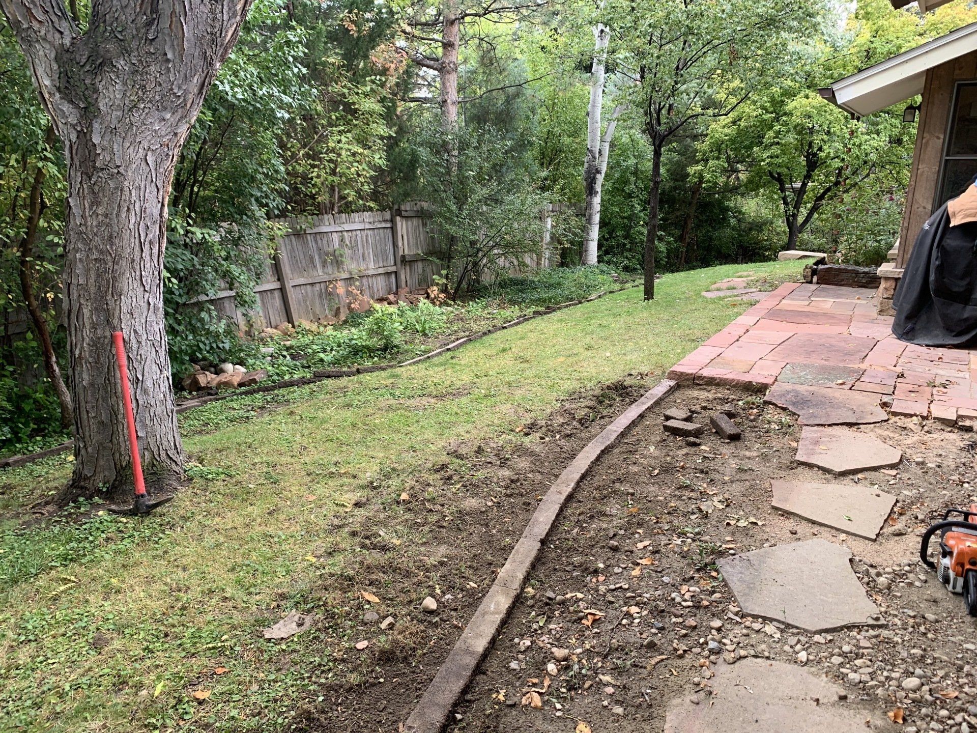 Backyard with a lawn, trees, a patio, and a wooden border.
