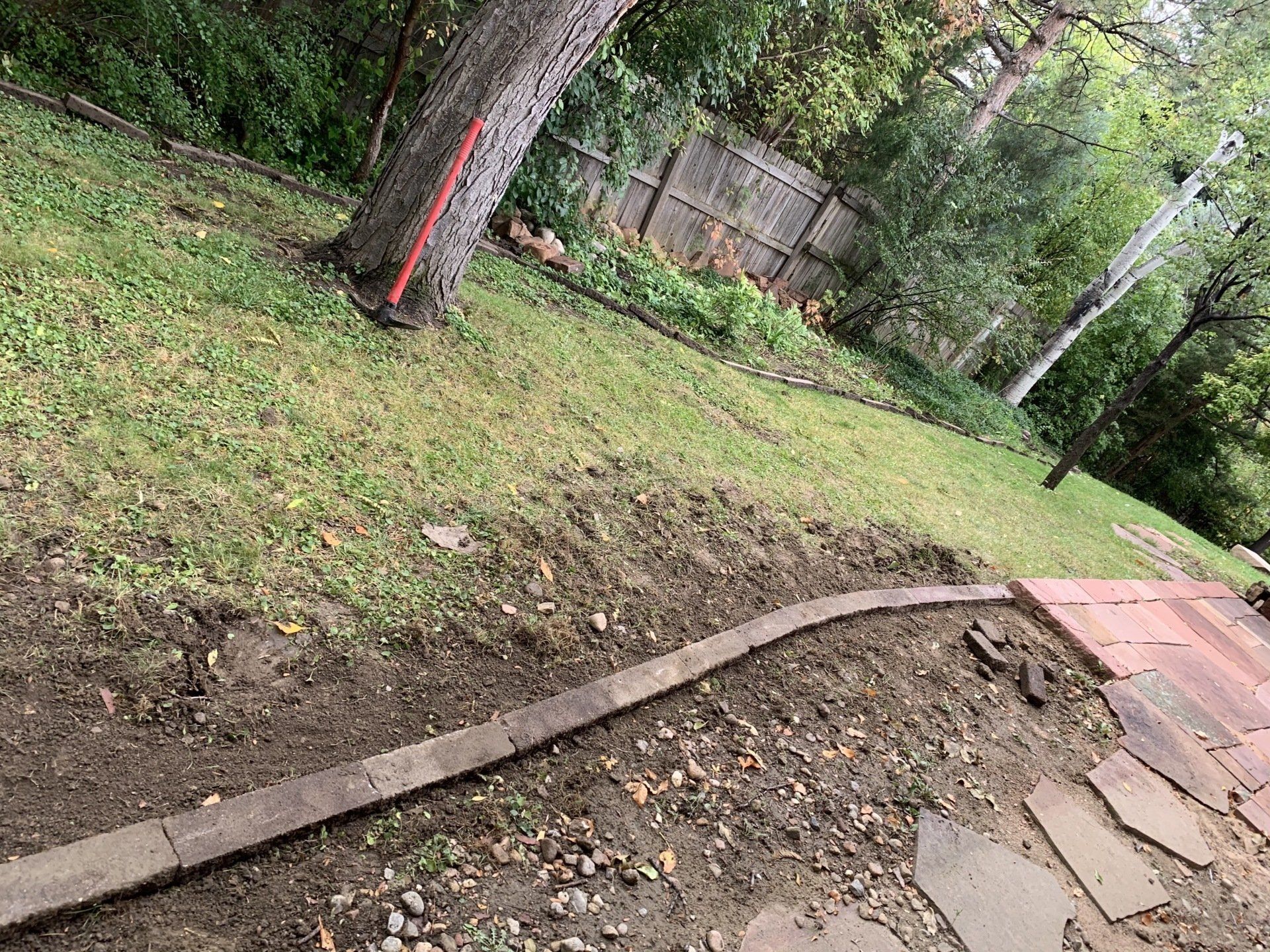 Dirt landscaping with a brick border on a grassy hill, tree in background.