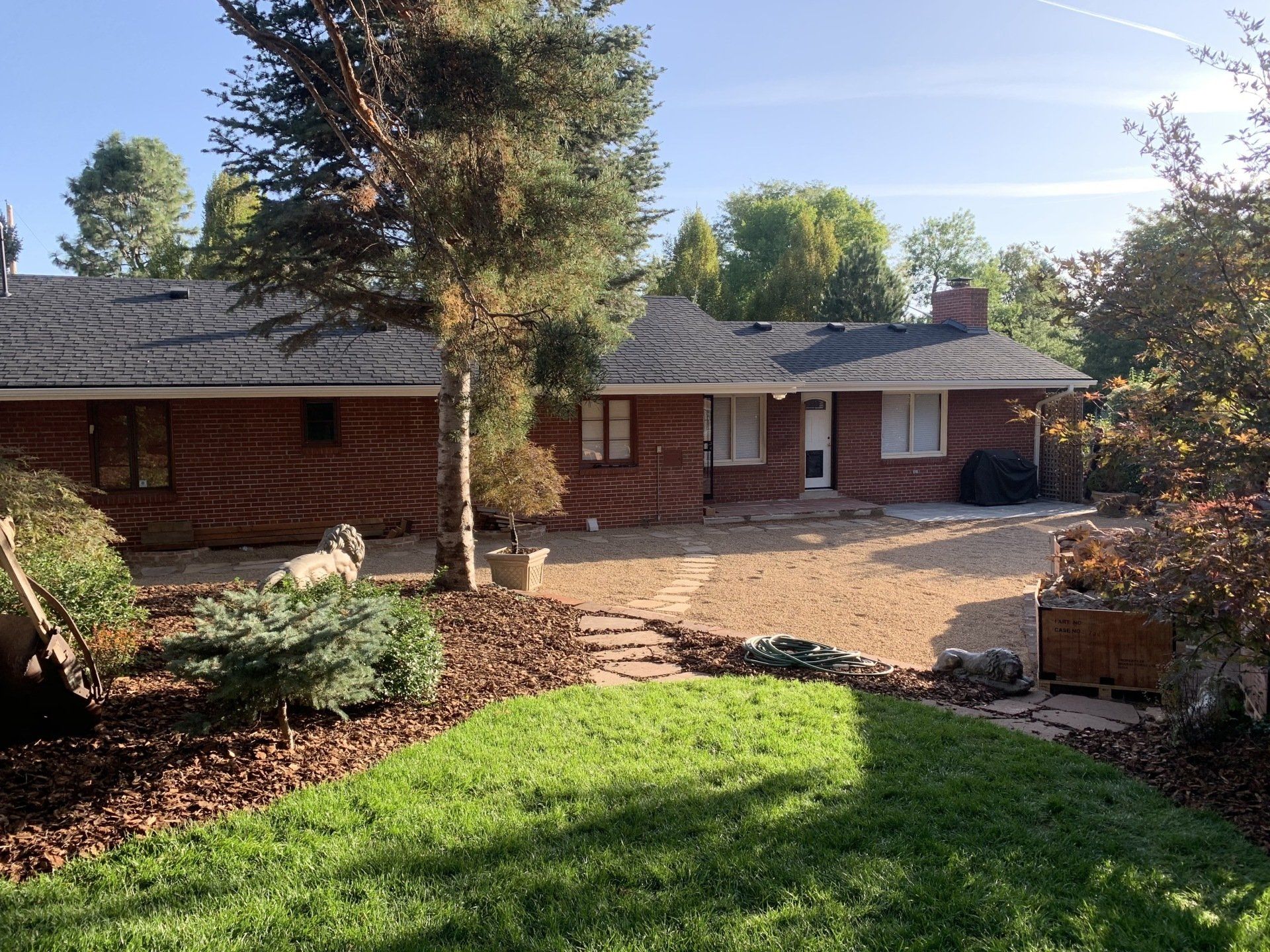 Brick house with a gravel patio and lawn, trees, and blue sky.