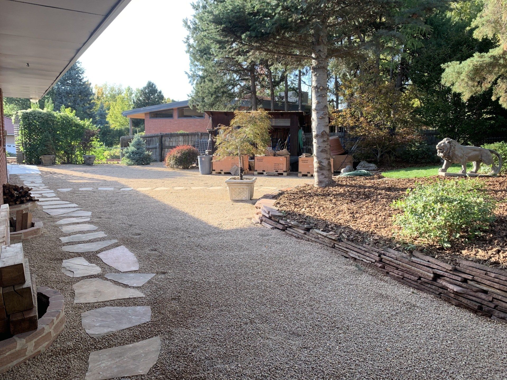 Gravel pathway and stepping stones lead to a house with a lion statue in a landscaped yard.