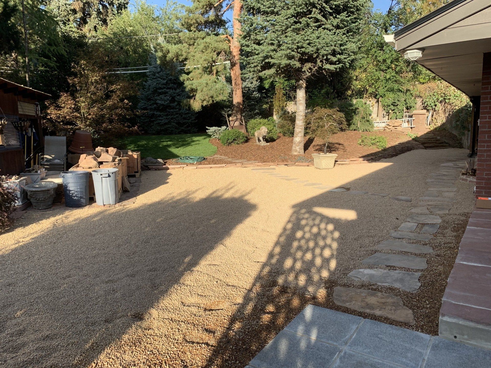 Gravel driveway with stepping stones, flanked by a building and landscaping, bathed in sunlight.