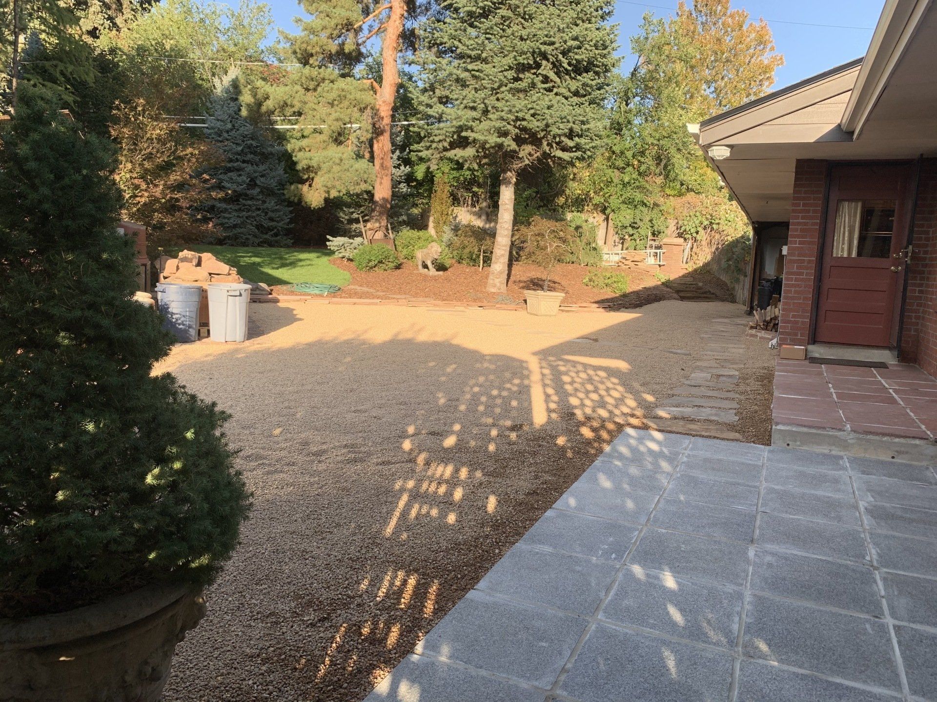Gravel driveway next to a brick building. Two evergreen trees frame the view.