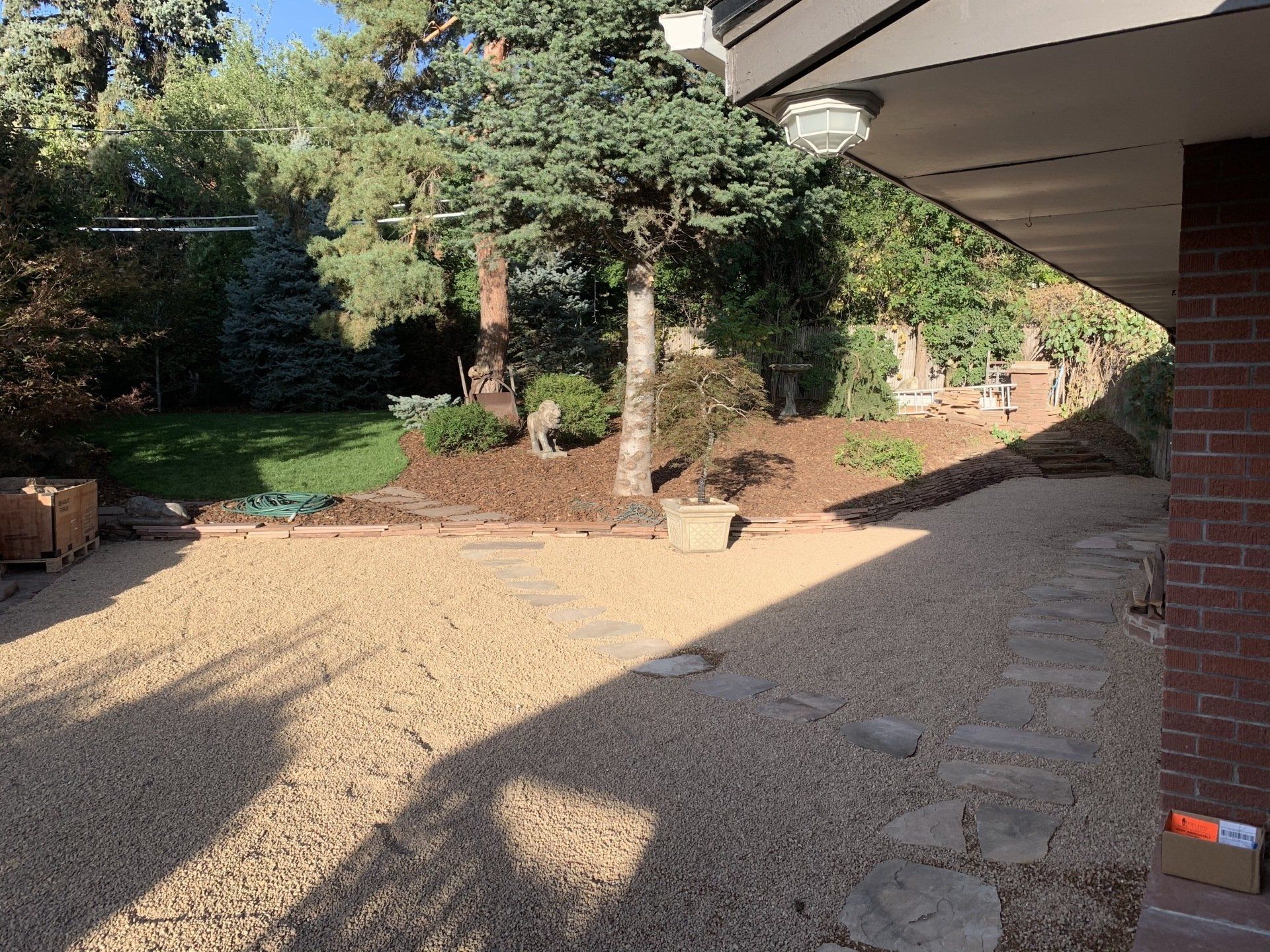 Backyard with gravel path, stepping stones, and trees. Sunny day.